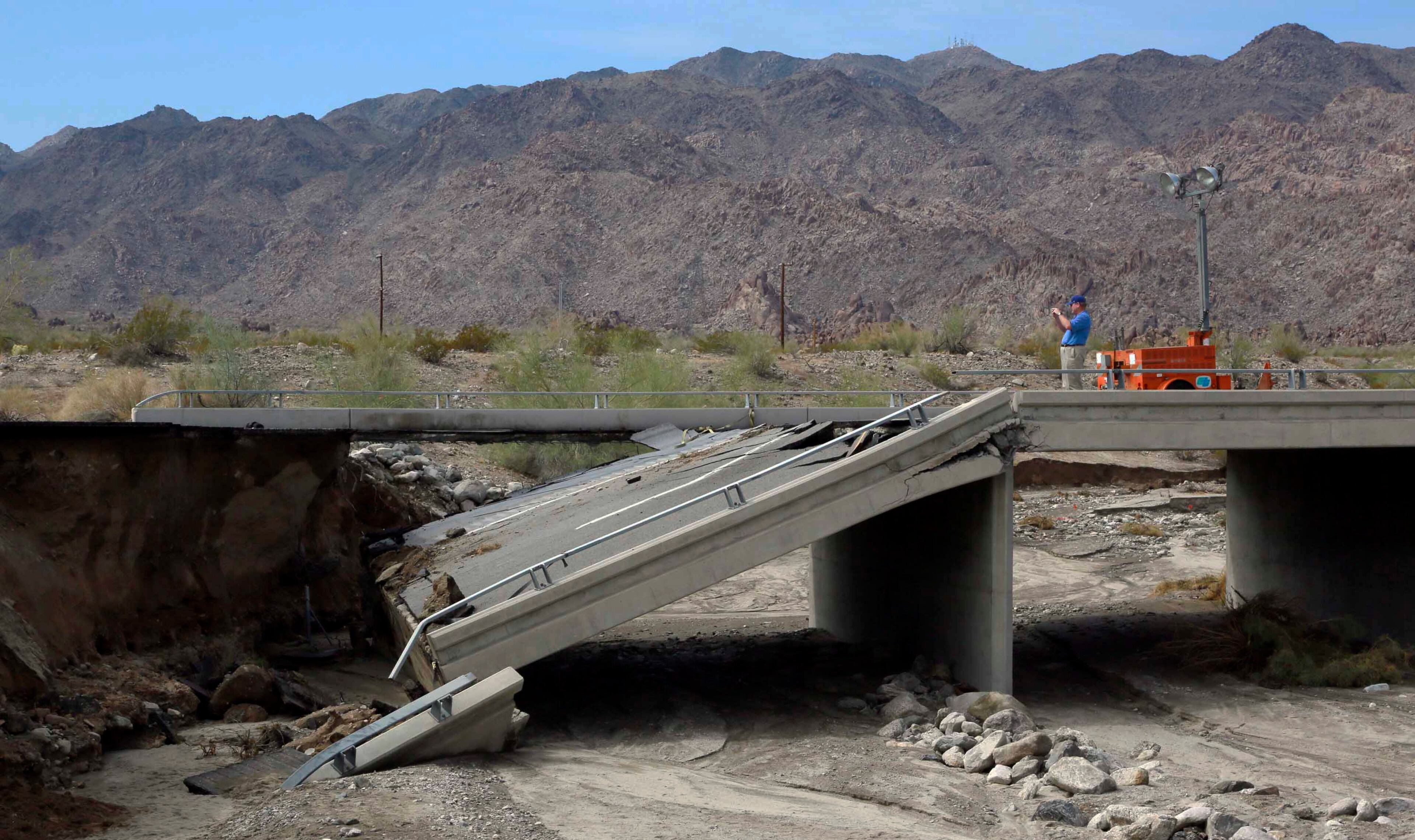 Riverside County Supervisor John J. Benoit takes a photo of a collapsed bridge that was washed out along Interstate 10 in Southern California, Monday, July 20, 2015. All traffic along one of the major highways connecting California and Arizona was blocked indefinitely when the bridge over a desert wash collapsed during a major storm, and the roadway in the opposite direction sustained severe damage. (AP Photo/Nick Ut)