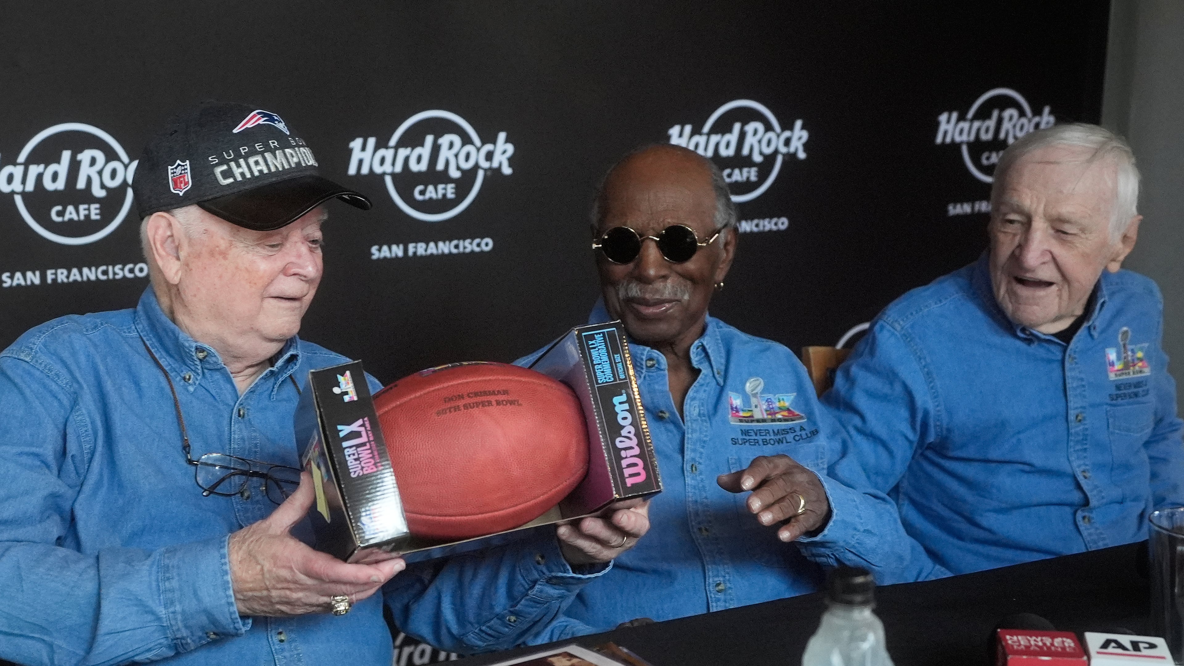 Don Crisman, left, holds up a Super Bowl LX football presented to he and friends Gregory Eaton, middle, and Tom Henschel, who have attended every Super Bowl football game by Wilson Sporting Goods, at a news conference at the Hard Rock Cafe in San Francisco, Friday, Feb. 6, 2026. (AP Photo/Jeff Chiu)