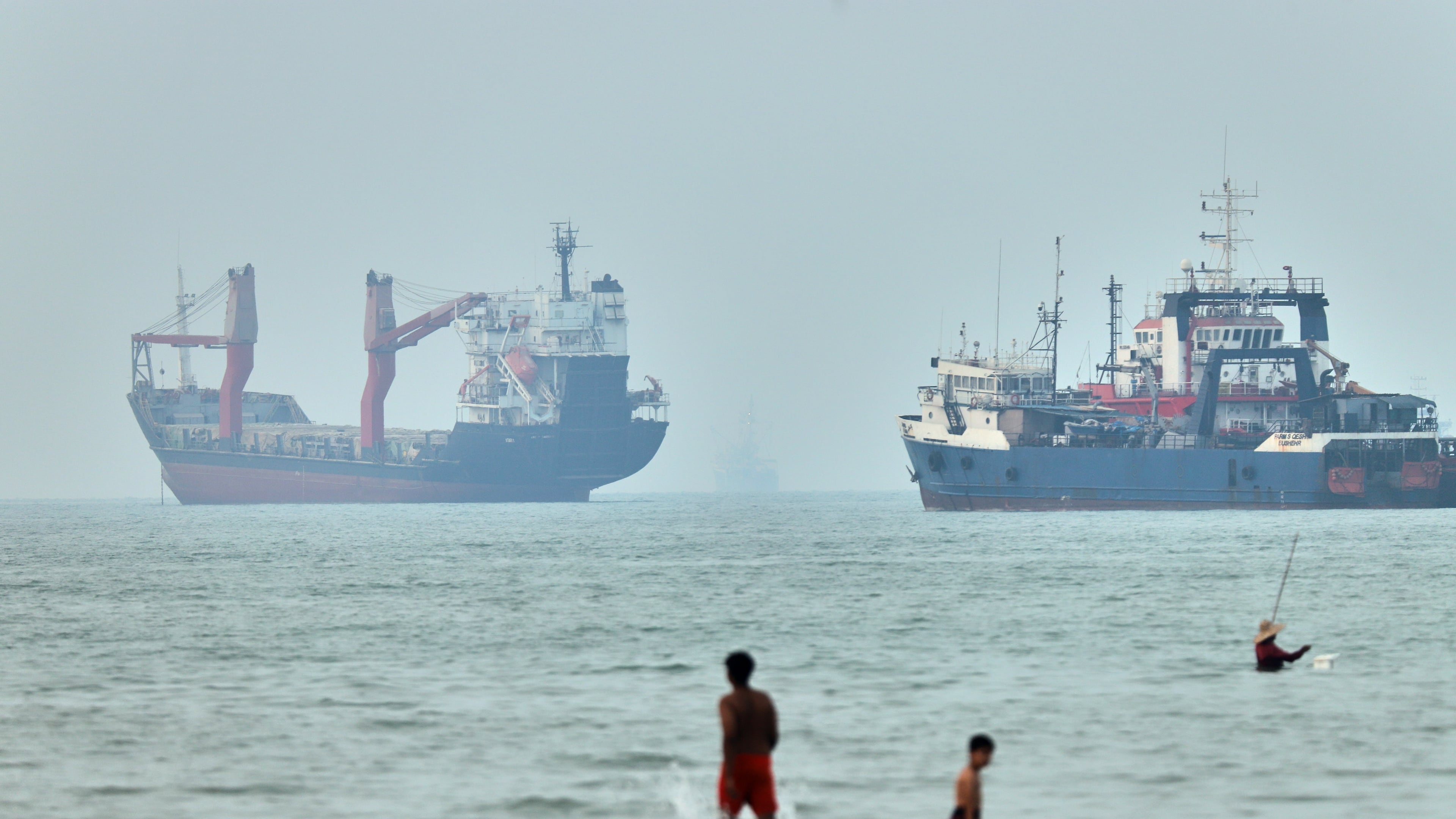 FILE - Children wade in the water with cargo ships at anchor in the background and a fisherman nearby, in the Strait of Hormuz off Bandar Abbas, Iran, Tuesday, June 30, 2026. (Amirhosein Khorgooi/ISNA via AP,File)