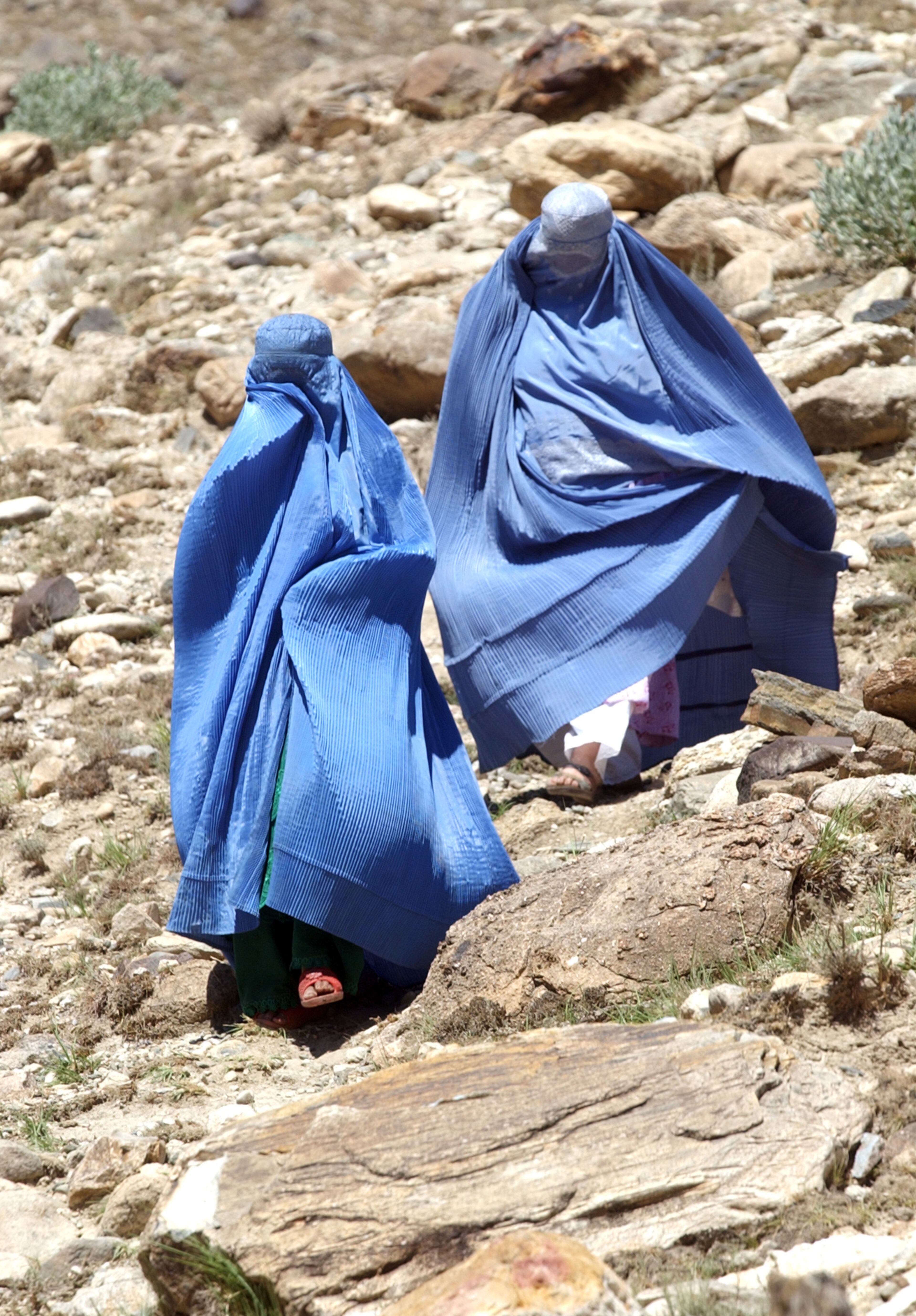 TORA BORA, AFGHANISTAN: Two Afghani women walk down a rocky hillside to visit a graveyard that has come to be considered a shrine to Islamic martyrdom for local residents of the Tora Bora area in Afghanistan Thursday, Sept. 5, 2002. (Bita Honarvar / The Atlanta Journal-Constitution)