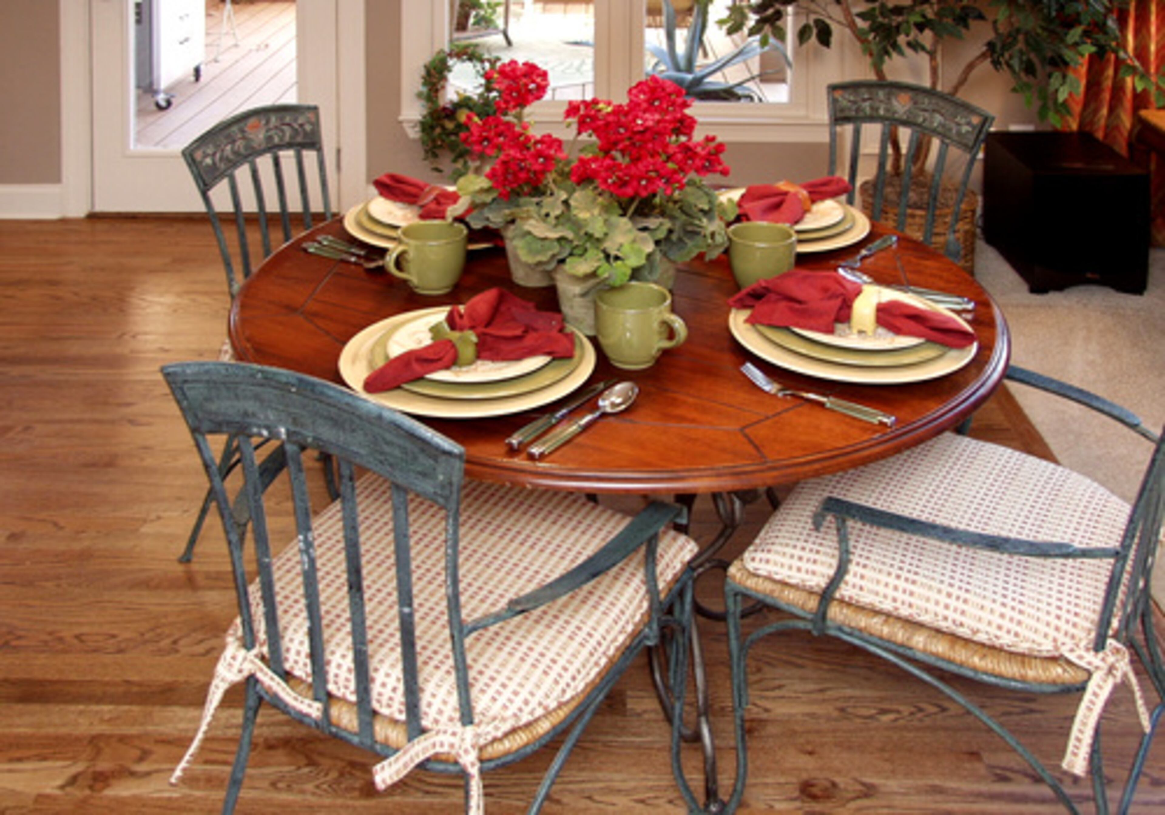 BREAKFAST AREA: Pots of red geraniums add pops of color to the neutral taupes and sage greens. The wrought-iron chairs have cushions in a textured fabric that pulls in the colors from the family room.