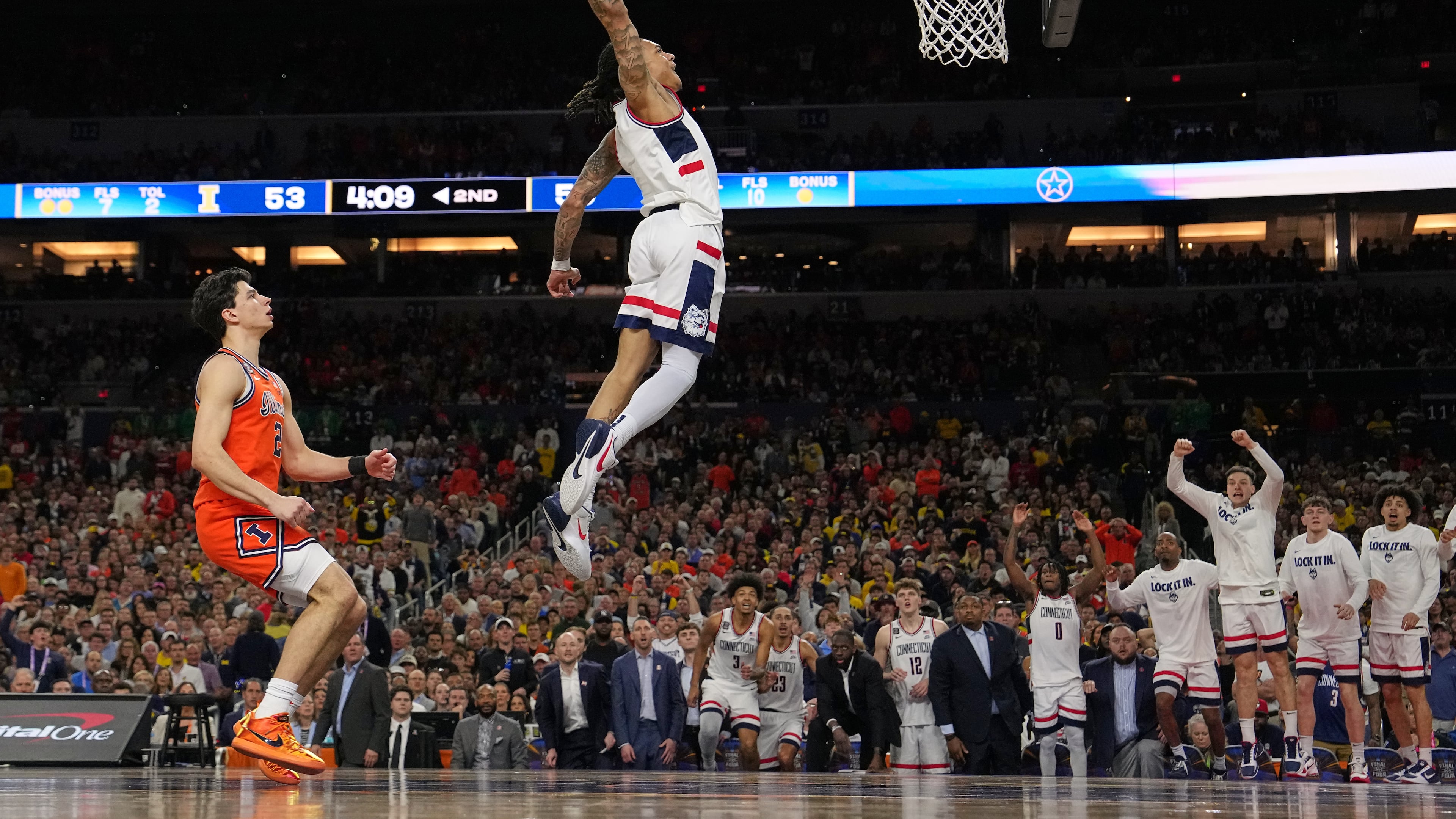 UConn's Solo Ball (1) dunks as Illinois' Andrej Stojakovic, left, watches during the second half of an NCAA college basketball tournament semifinal game at the Final Four, Saturday, April 4, 2026, in Indianapolis. (AP Photo/Michael Conroy)