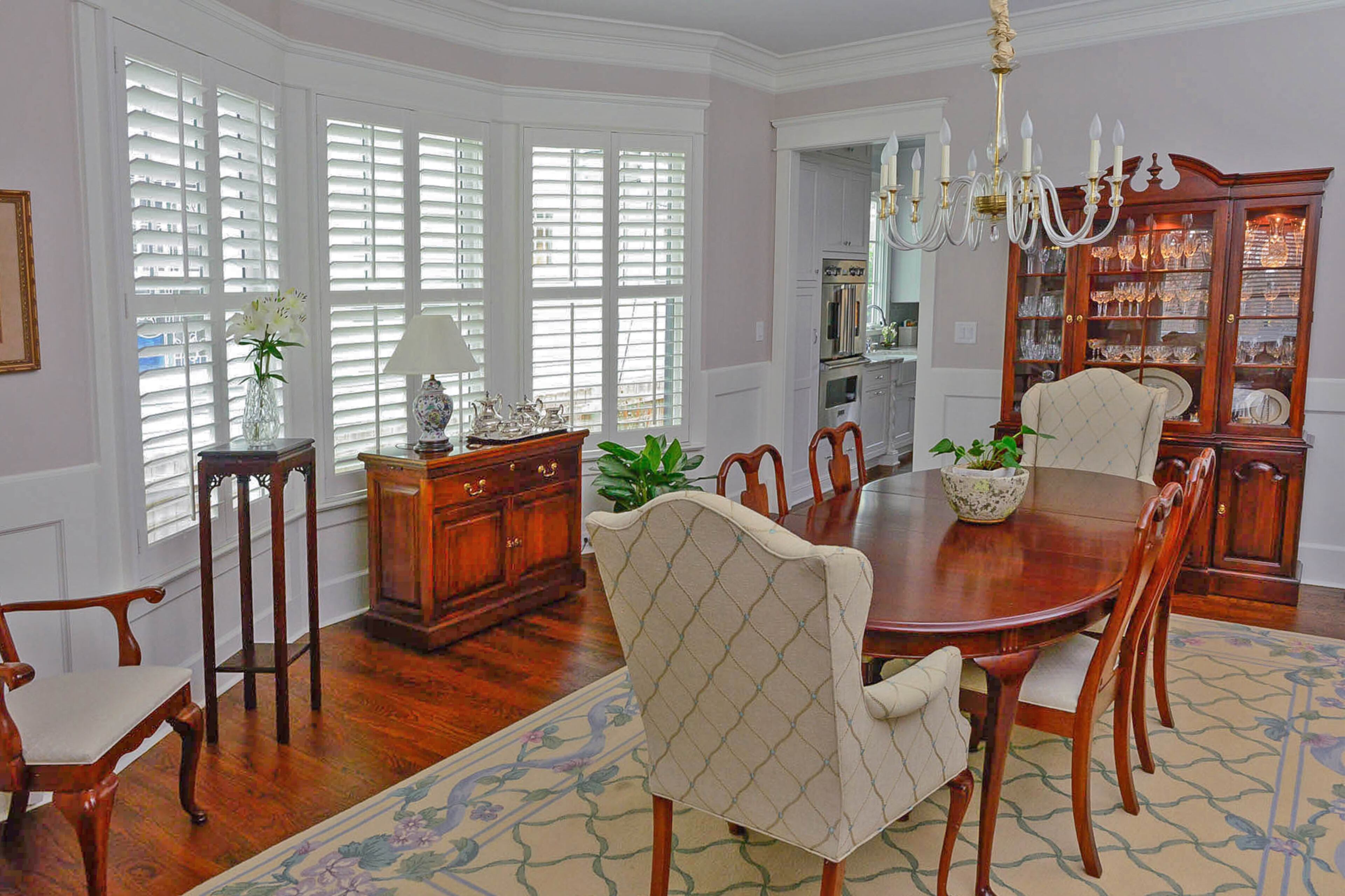 A highlight of the dining room is the Murano glass chandelier from The Big Chandelier. A flower and vine trellis rug complements the pattern on the upholstered chairs. The walls are painted Pediment by Sherwin-Williams.