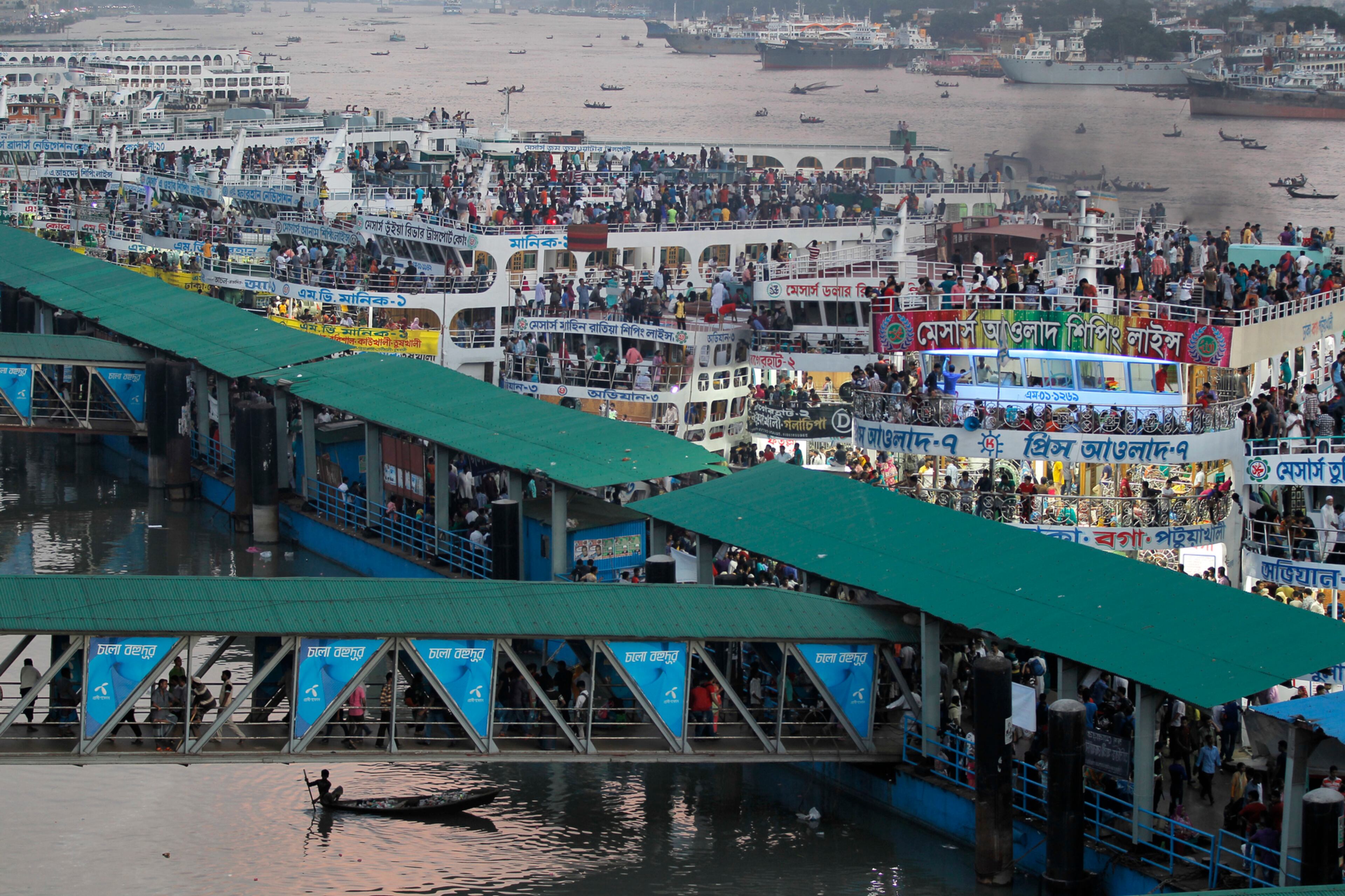A boy rows a boat, bottom left, past a ferry terminal crowded with people traveling to their hometowns for Eid al-Adha festival in Dhaka, Bangladesh, Friday, Sept. 9, 2016. Muslims around the world celebrate Eid al-Adha, or the Feast of the Sacrifice, to commemorate the prophet Ibrahim's faith in being willing to sacrifice his son. (AP Photo/A.M. Ahad)