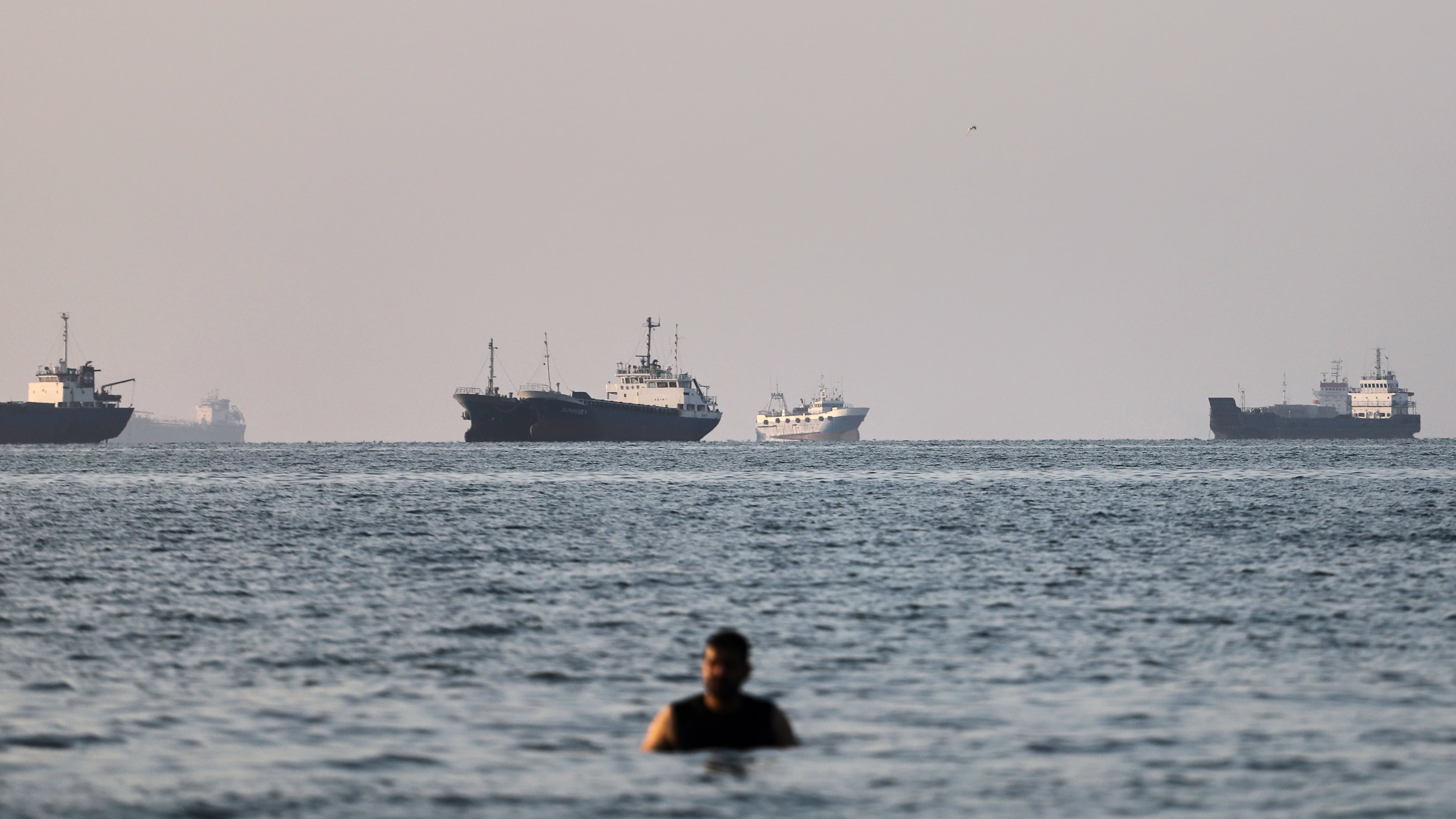 A person stands in shallow water as cargo and commercial vessels are anchored in the Strait of Hormuz off Bandar Abbas, Iran, Monday, June 8, 2026. (Amirhosein Khorgooi/ISNA via AP)