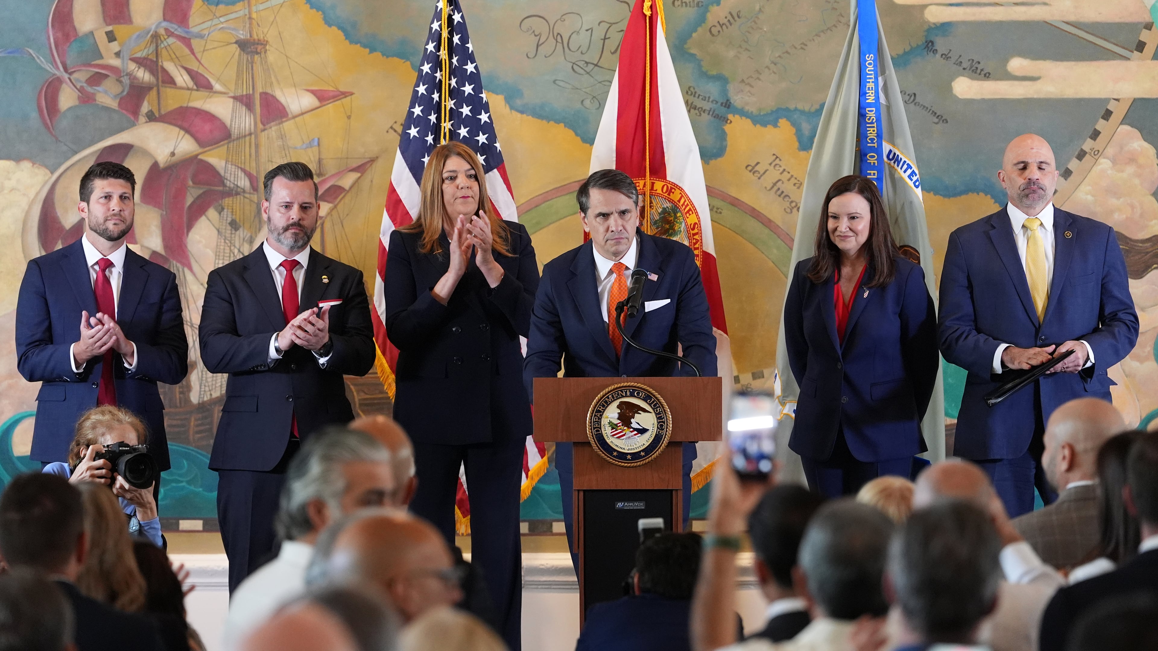 Audience members give a standing ovation as Acting Attorney General Todd Blanche, center, speaks at an event where federal prosecutors announced charges against former Cuban President Raul Castro in the 1996 downing of civilian planes operated by Miami-based exiles, Wednesday, May 20, 2026, in Miami. Also shown, from left, are, Florida Attorney General James Uthmeier; Jason A. Reding Quiñones, U.S. attorney for the southern district of Florida; Miami Dade College President Madeline Pumariega; Sen. Ashley Moody, R-Fla.; and FBI Deputy Director Christopher Raia. (AP Photo/Rebecca Blackwell)