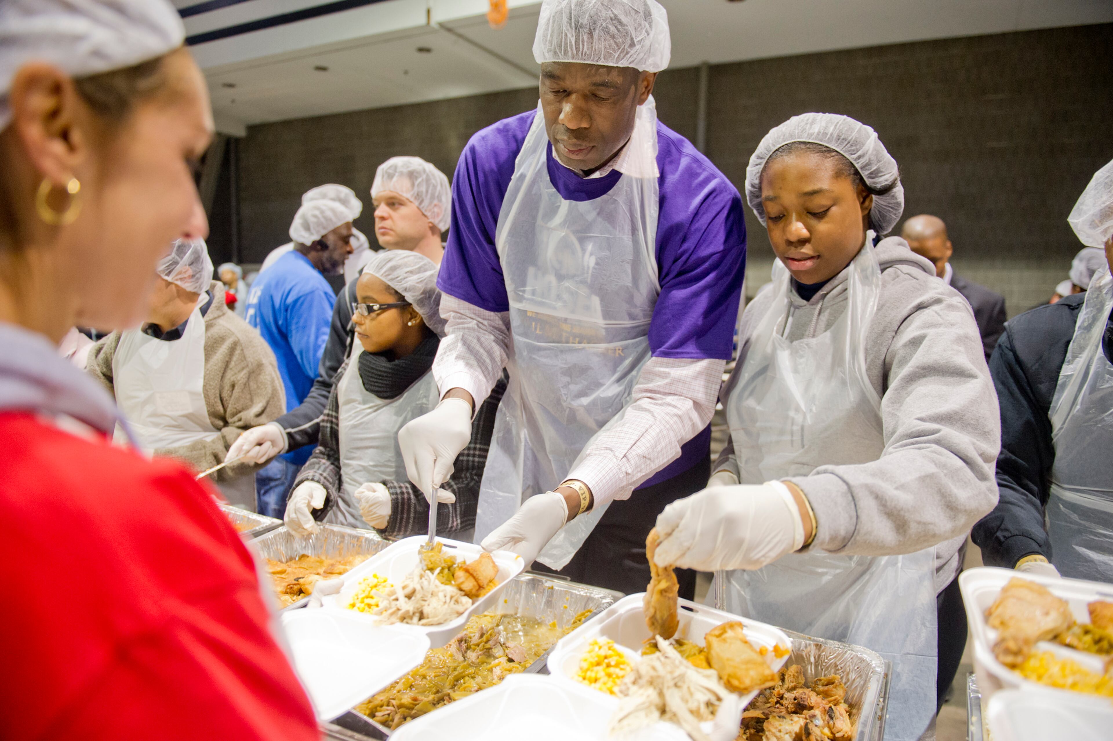 Dikembe Mutombo (center) and his daughter Carrie put food on trays during the Hosea Feed the Hungry and Homeless annual Thanksgiving meal at the Georgia World Congress Center in Atlanta on Nov. 28, 2013.