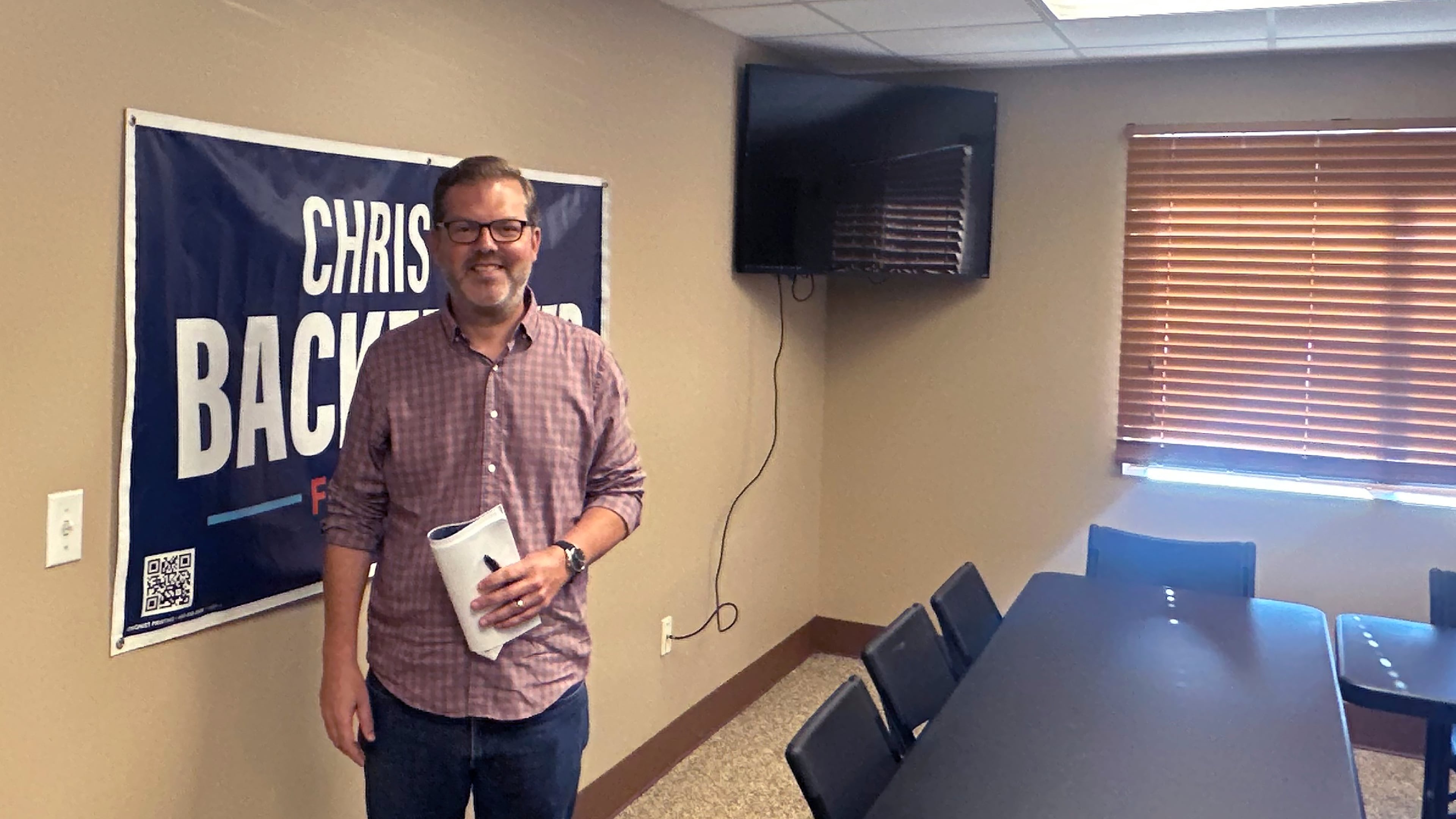Democratic congressional candidate Chris Backemeyer poses in front of a campaign banner after an event in Murdock, Nebraska, on Sunday, Aug. 16, 2026. (AP Photo/Will Weissert)