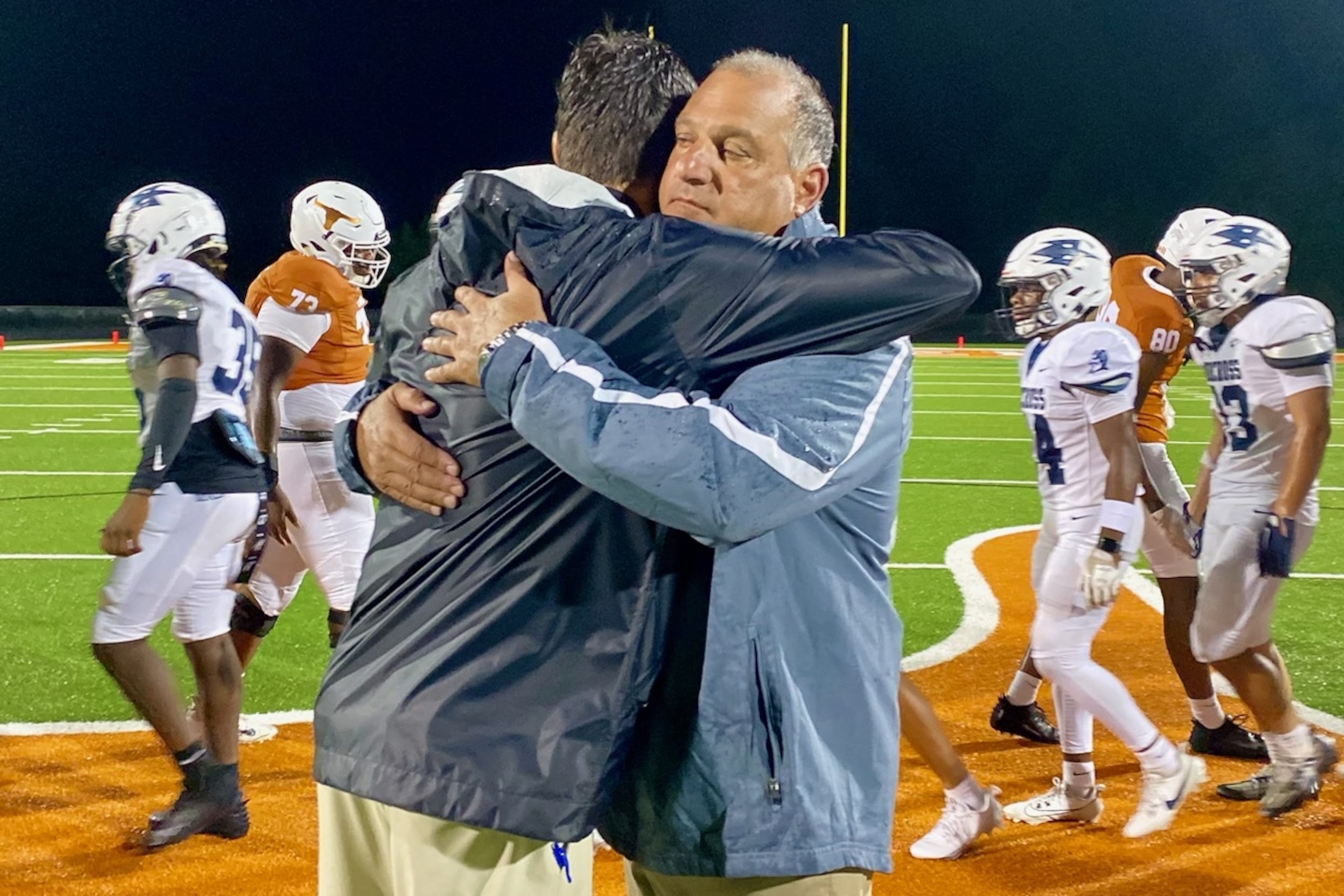 Norcross High coach Keith Maloof hugs his son Tyler Maloof, the coach at Lanier High, after the Blue Devils’ 31-10 win on Friday, Aug. 16, 2024. It was the first father-son coaching matchup in GHSA football since 2006. (Ken Sugiura/AJC 2024)