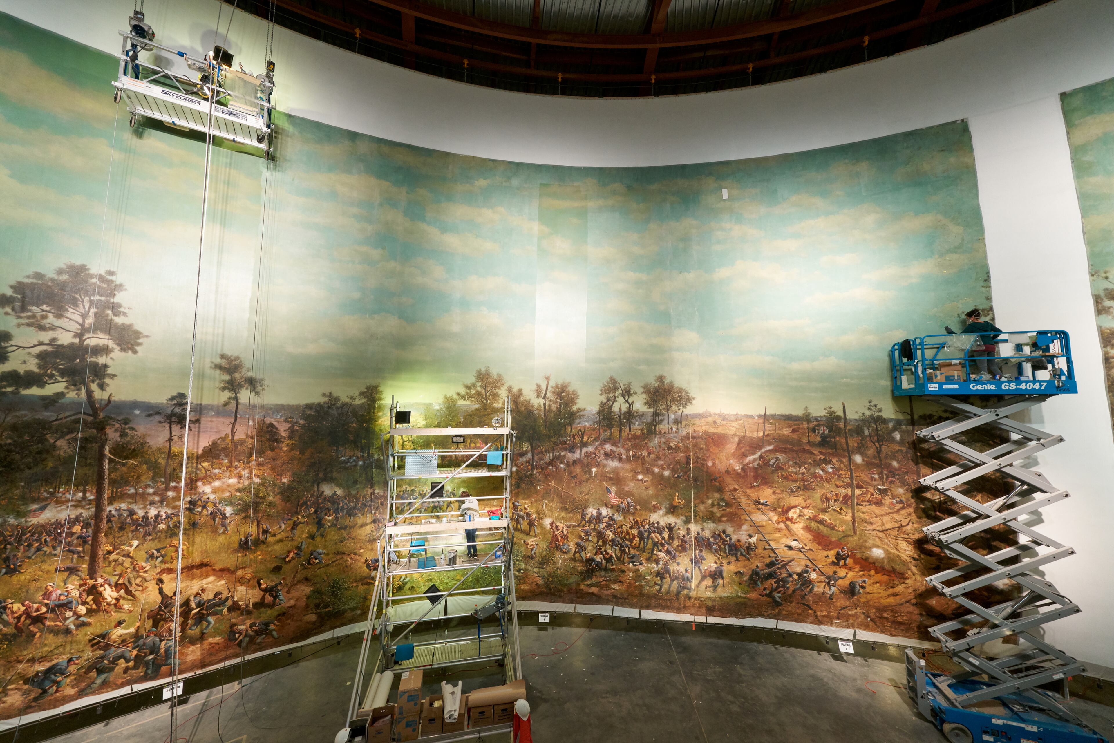 Conservators on scissor lifts complete the restoration of “The Battle of Atlanta,” including adding back one of the vertical sections that was missing, seen at right. Artisans used chopsticks wrapped with cotton bolls to clean the mammoth painting. CONTRIBUTED: ATLANTA HISTORY CENTER