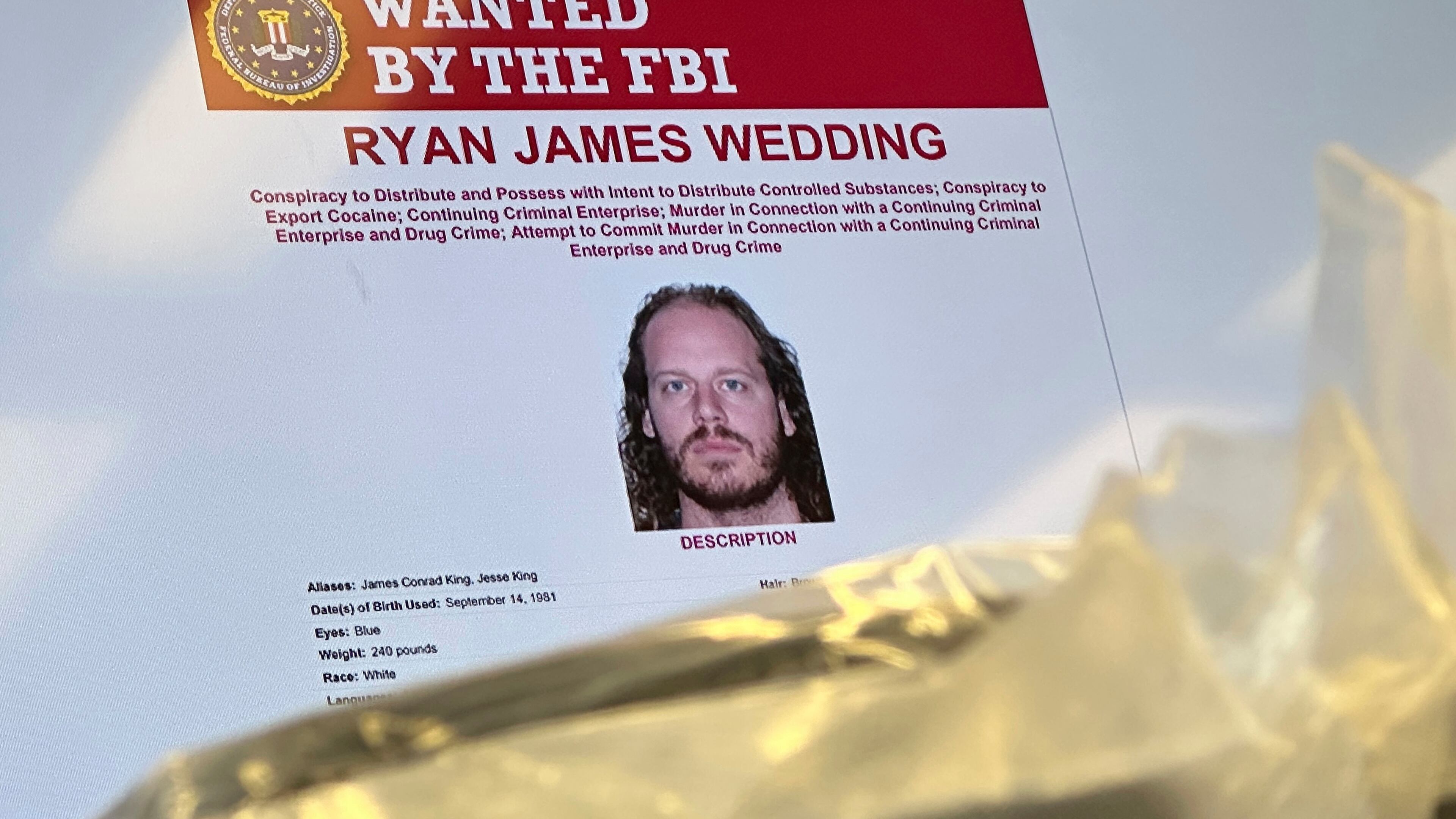 FILE - An image of former Canadian Olympic snowboarder Ryan Wedding, who is a fugitive and been charged with allegedly running and participating in a transnational drug trafficking operation, is displayed on a video monitor along with bricks of cocaine, foreground, during a news conference at the FBI offices in Los Angeles, Oct. 17, 2024. (AP Photo/Damian Dovarganes, File)