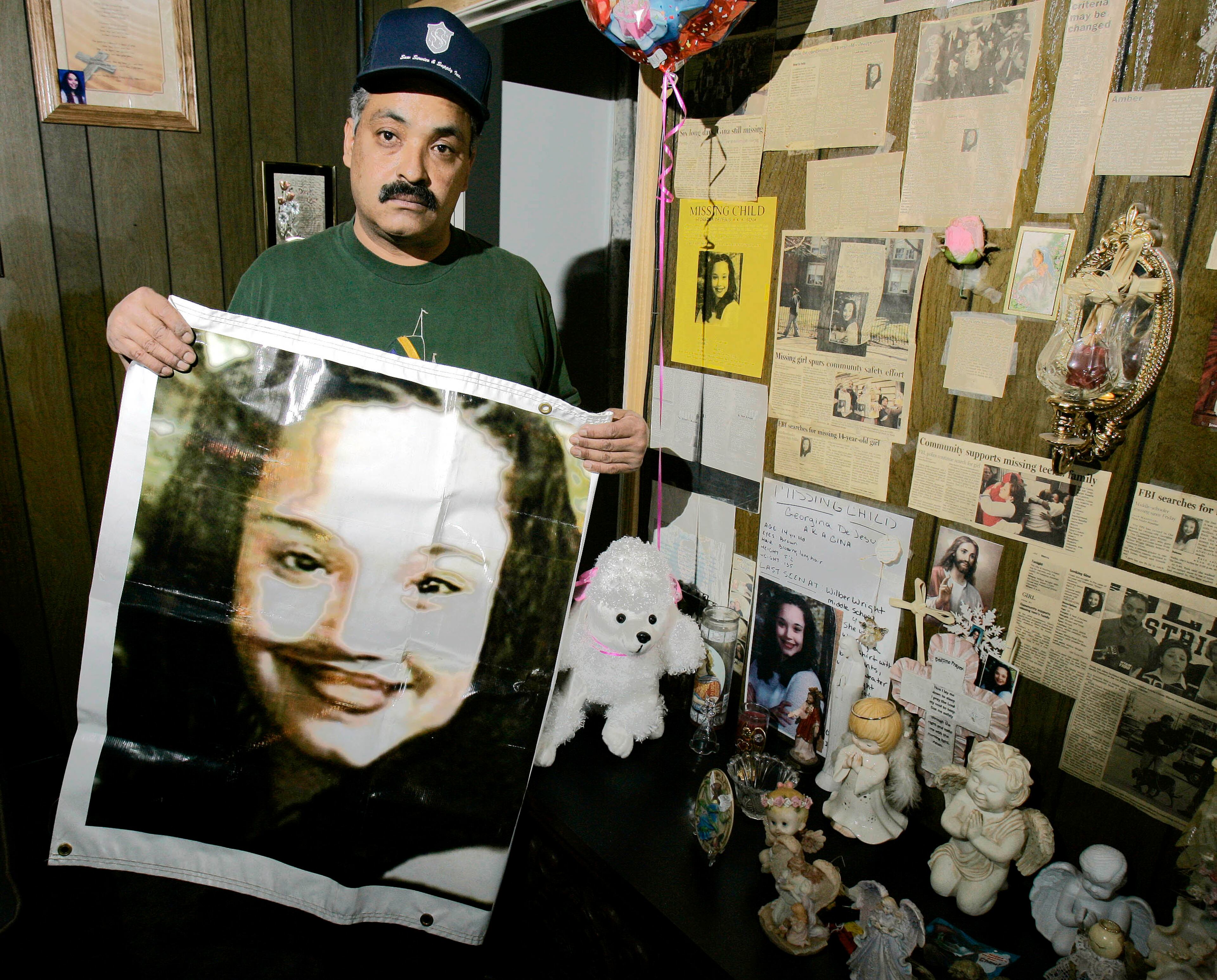 In this Friday, March 3, 2004 file photos shows Felix DeJesus, holding a banner showing his daughter's photograph, standing by a memorial in his living room in Cleveland. Cleveland police say two women who went missing as teenagers about a decade ago have been found alive in a residential area about two miles south of downtown. Cheering crowds gathered Monday night on the street near the home where police say Amanda Berry, Gina DeJesus and a third woman were found earlier in the day. The identity of the third woman hasn't been confirmed. (AP Photo/Tony Dejak, File)