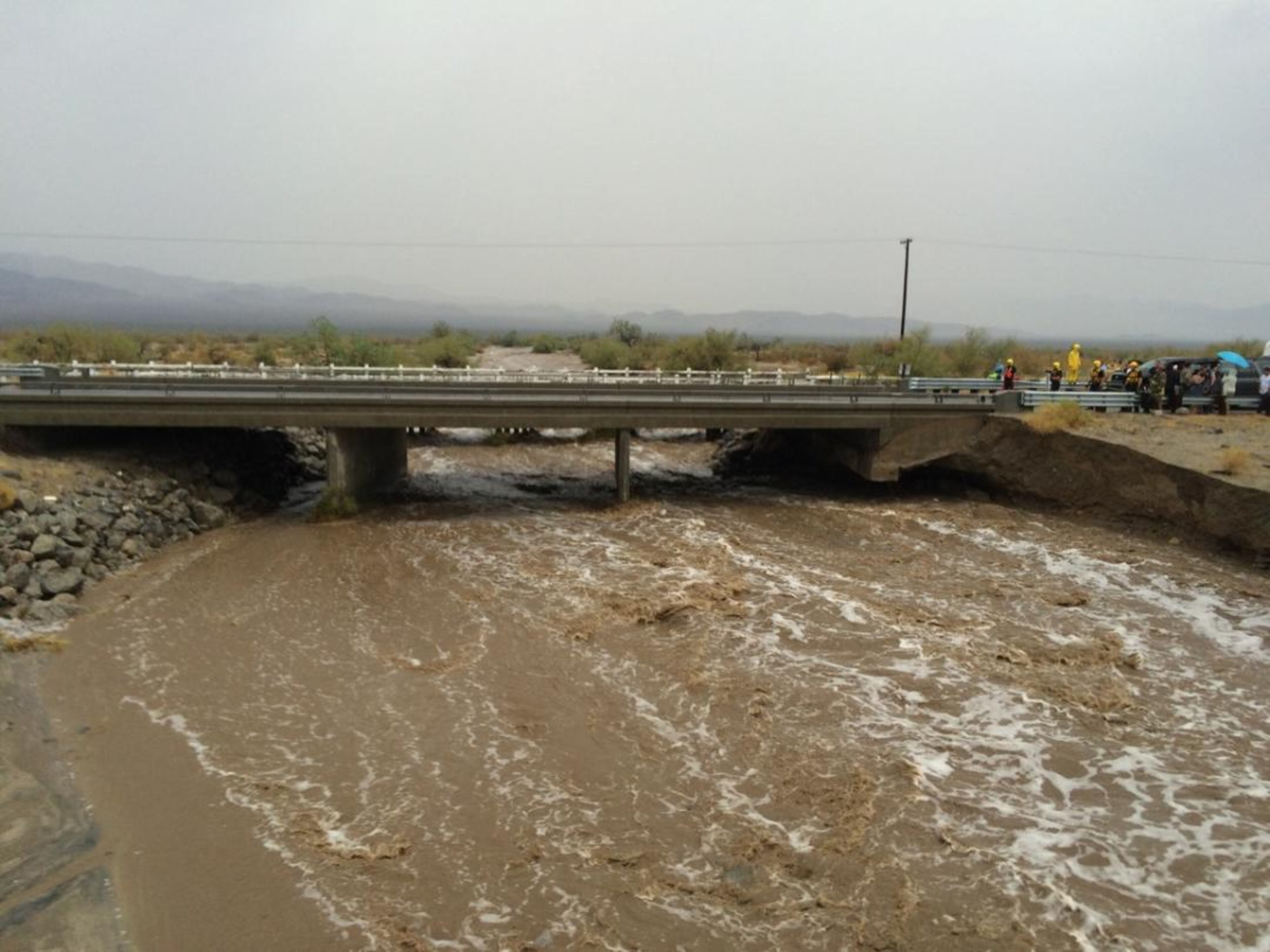 In this photo provided by the CAL FIRE/Riverside County Fire Department, waters rush under an the elevated portion westbound Interstate 10 as emergency crews respond to the collapse of the eastbound section, Sunday, July 19, 2015, in Desert Center, Calif. The bridge, which carries the eastbound interstate about 15 feet above a normally dry wash, snapped and ended up in the flooding water below, the California Highway Patrol said, blocking all traffic headed toward Arizona. (Chief Geoff Pemberton/CAL FIRE/Riverside County Fire via AP)