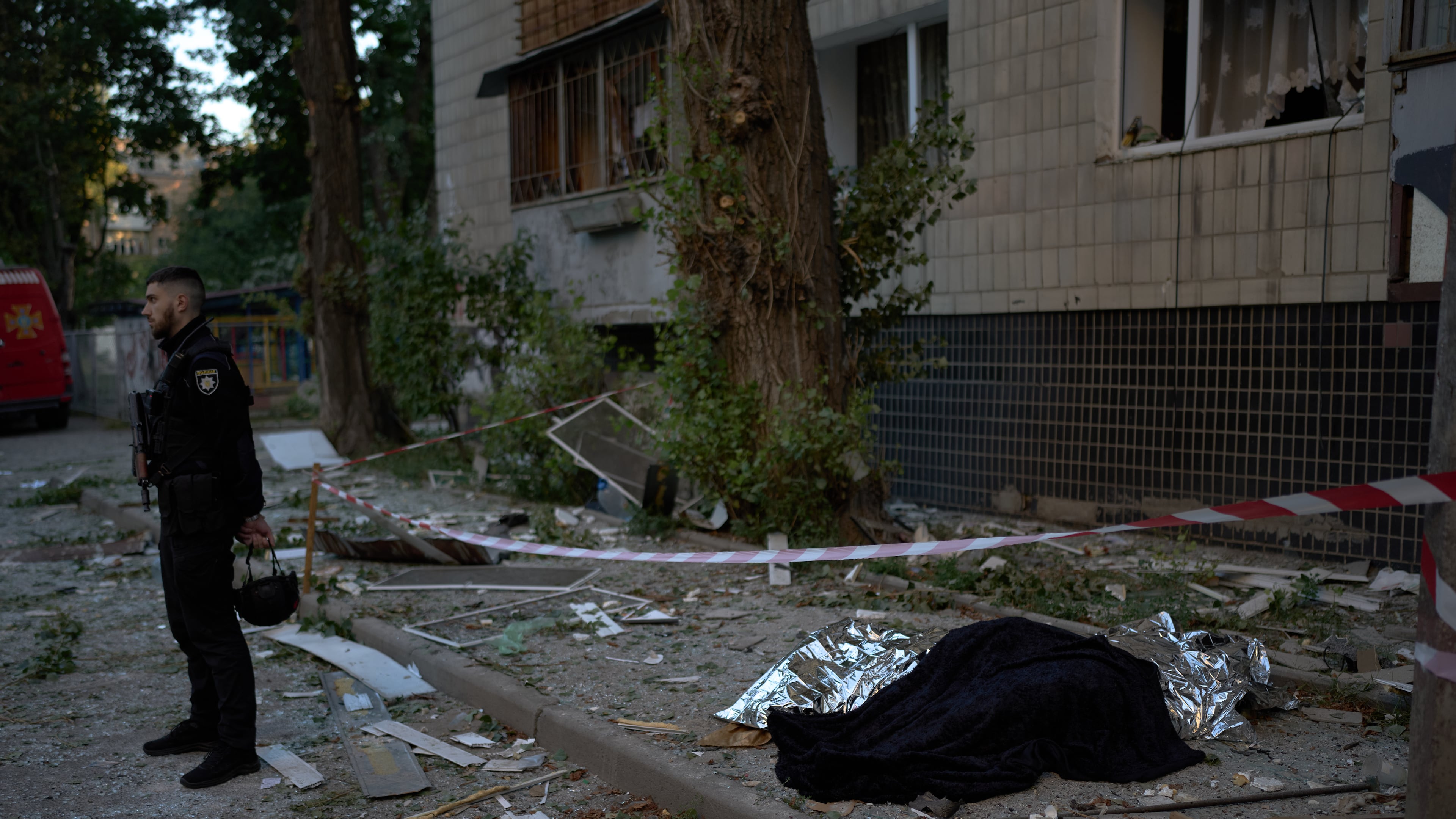 A policeman stands next to the bodies of two people killed during an overnight Russian attack in Kyiv, Ukraine, Thursday, Aug. 20, 2026. (AP Photo/Francisco Seco)