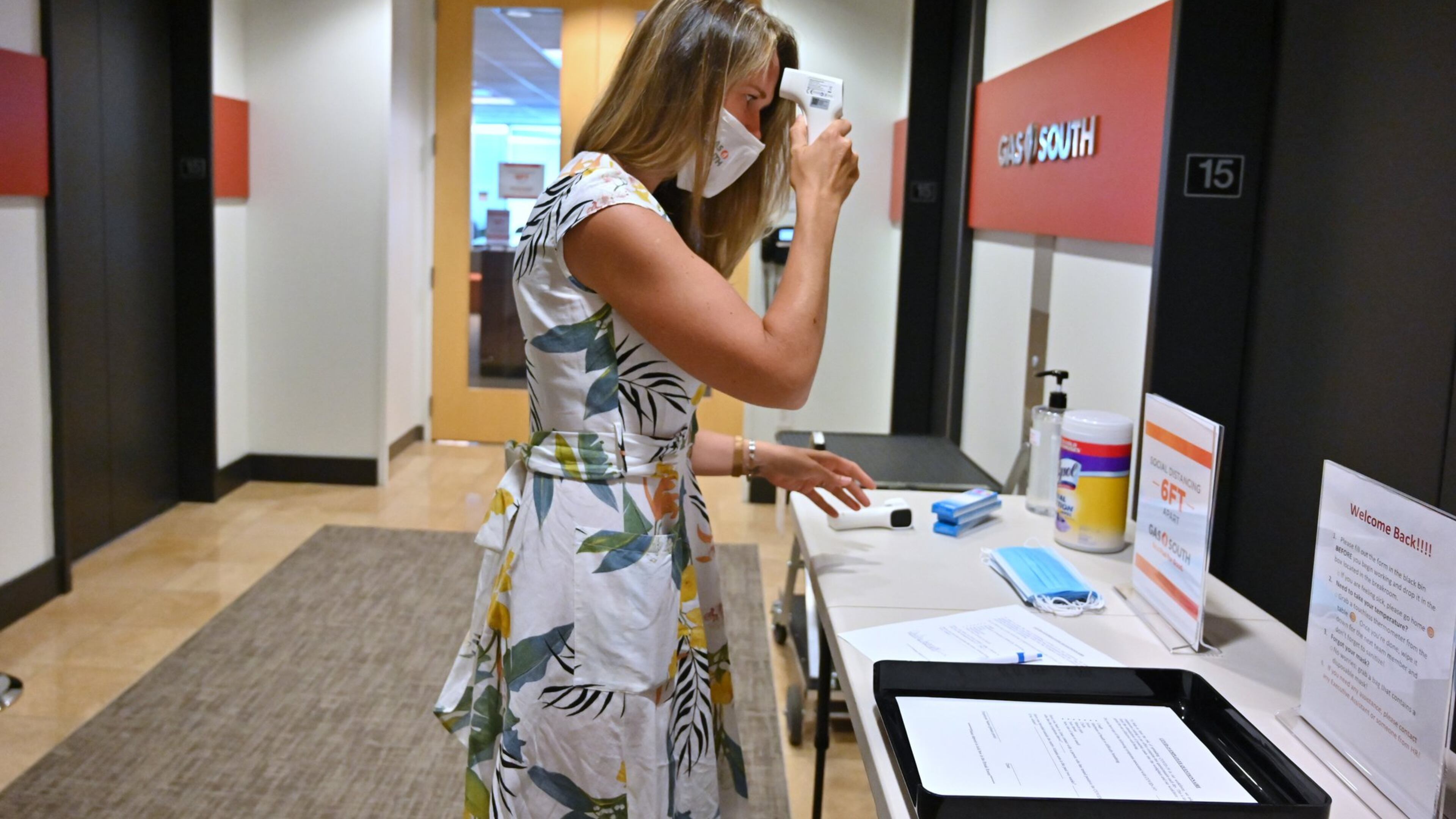 Carley Stephens, a community affairs manager at Gas South, checks her temperature before she walks into the company’s offices in Cobb County. Shoppers are hitting stores and filling parking lots. Some diners are returning to sit-down restaurants. But many of metro Atlanta’s white-collar towers and office parks are still lonely places as people work remotely during the coronavirus pandemic. (Hyosub Shin / Hyosub.Shin@ajc.com)