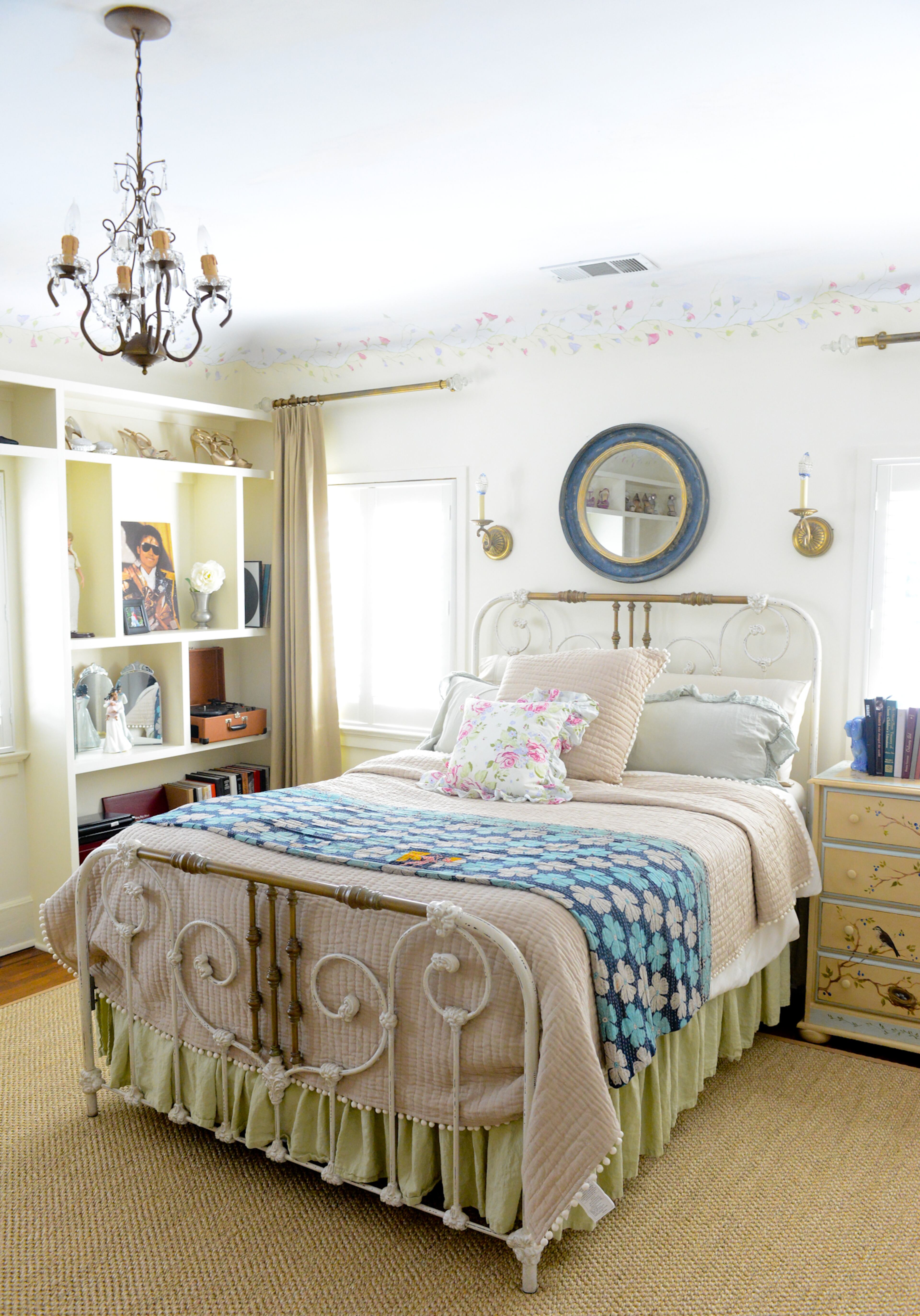 A traditional interior style is showcased in their daughter's bedroom upstairs. The classic brass bed is flanked with wall sconces and soft creams and pastels are used in the antiqued furniture, built-in bookshelves and bed linens.
