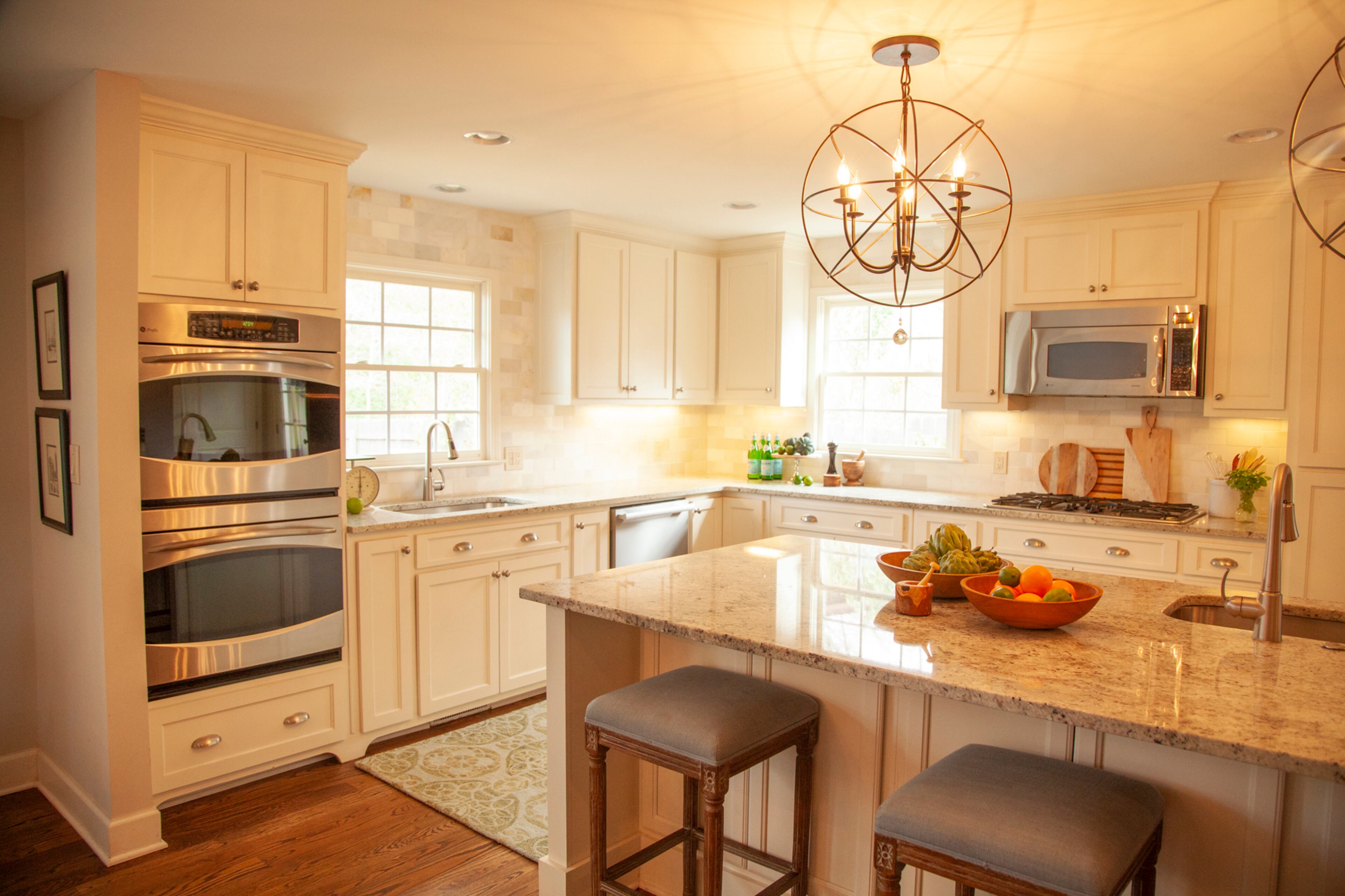 Carrera marble subway tile used for the backsplash carries the tones found in the Colonial White granite countertops. Lighting is from Ballard Designs. The renovated space has double ovens and dishwashers. Text by Kat Khoury/Fast Copy News Service. Photo by Reann Huber/Fast Copy News Service.