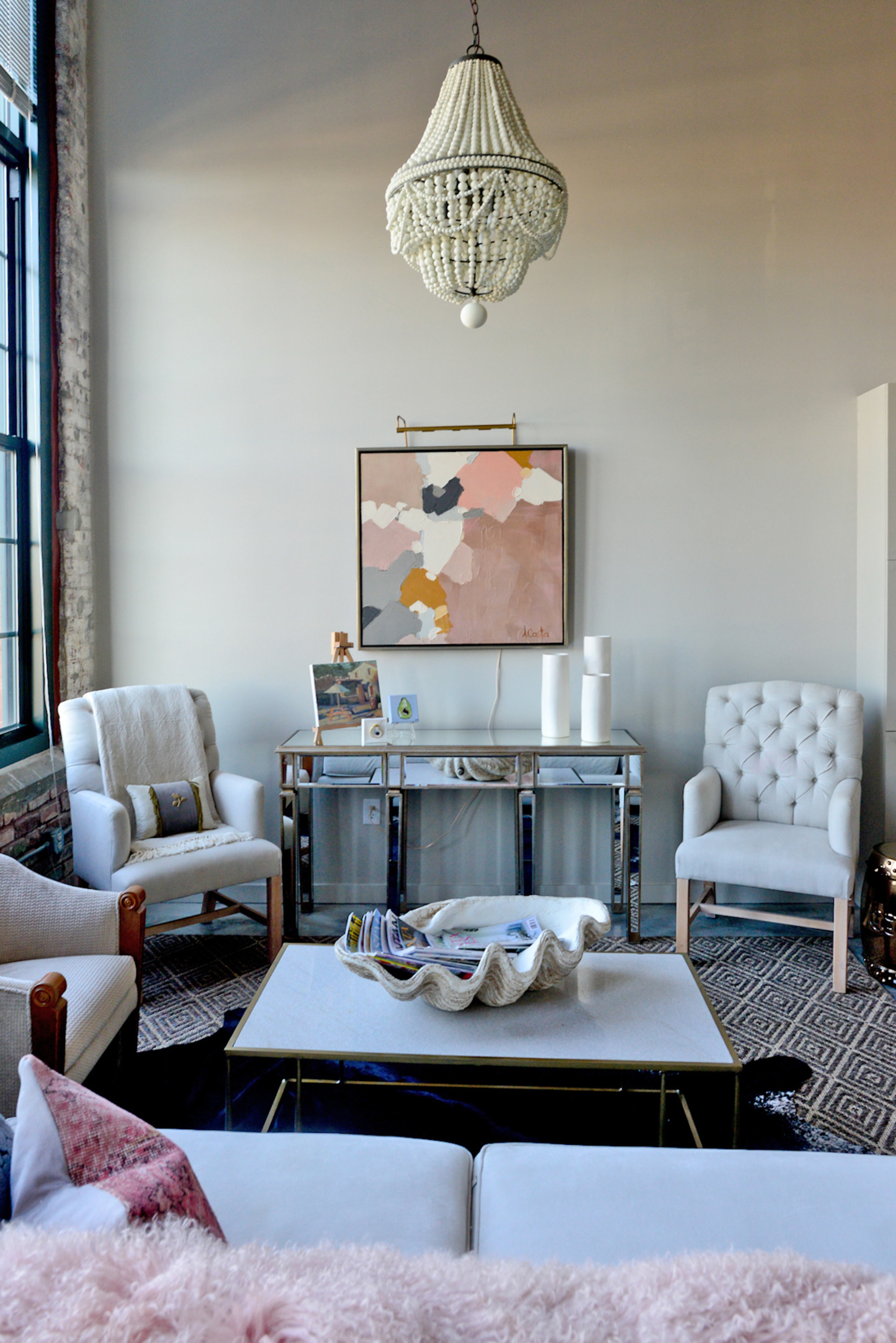 The walls and soaring ceilings allows Andrea Costa to display statement pieces, like the beaded chandelier by Regina Andrew Design and original art, including her work and pieces by artists Hannah Stettner of Stett Studio, Dawne Raulet and Donna Hughes. The sofa and coffee table are from Gregory Joseph Designs/Westside Market.