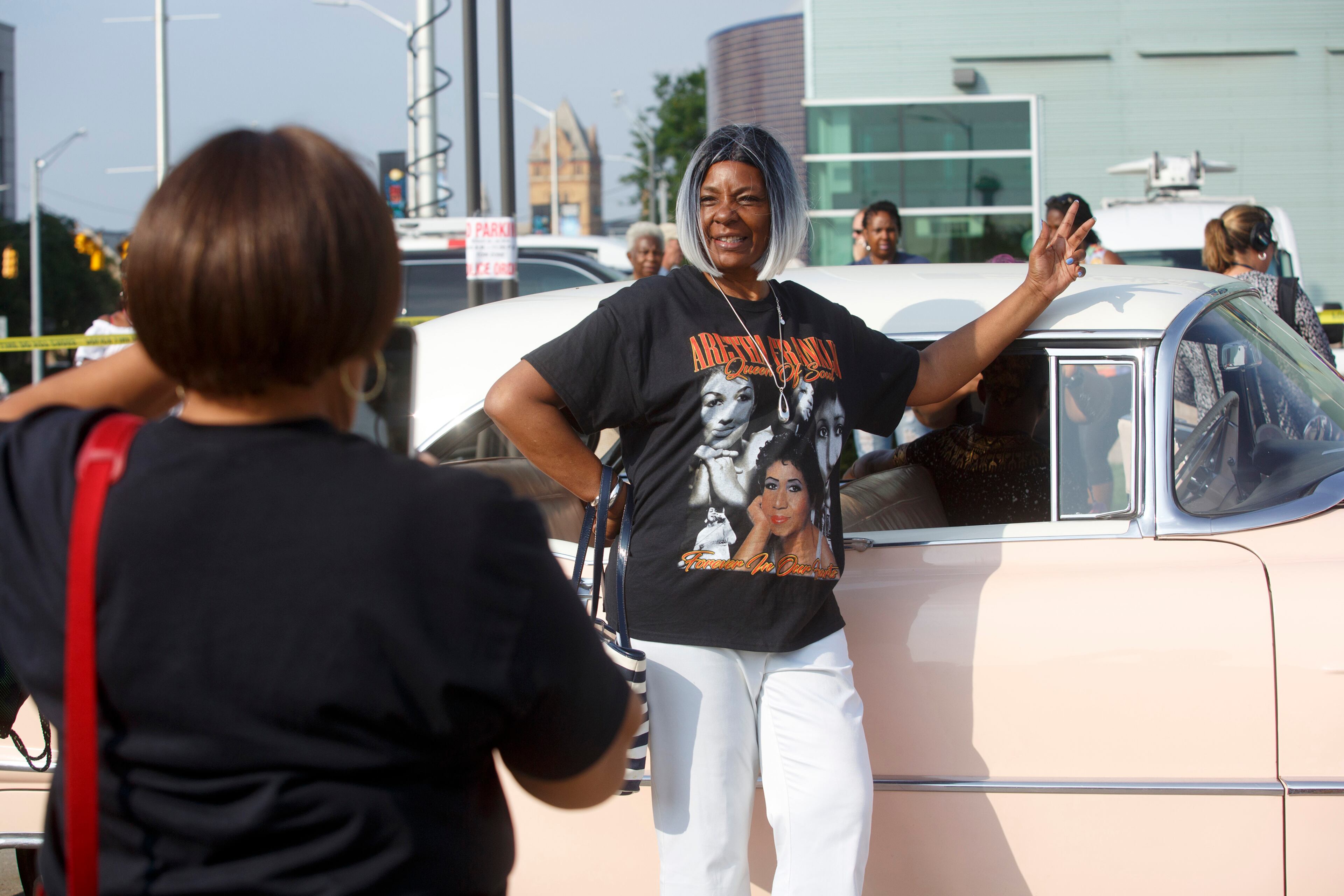 A woman poses for a photo with a pink Cadillac parked in front of the Charles H. Wright Museum of African American History in honor of a public viewing of Aretha Franklin, in Detroit, Aug. 28, 2018. (Laura McDermott/The New York Times)
