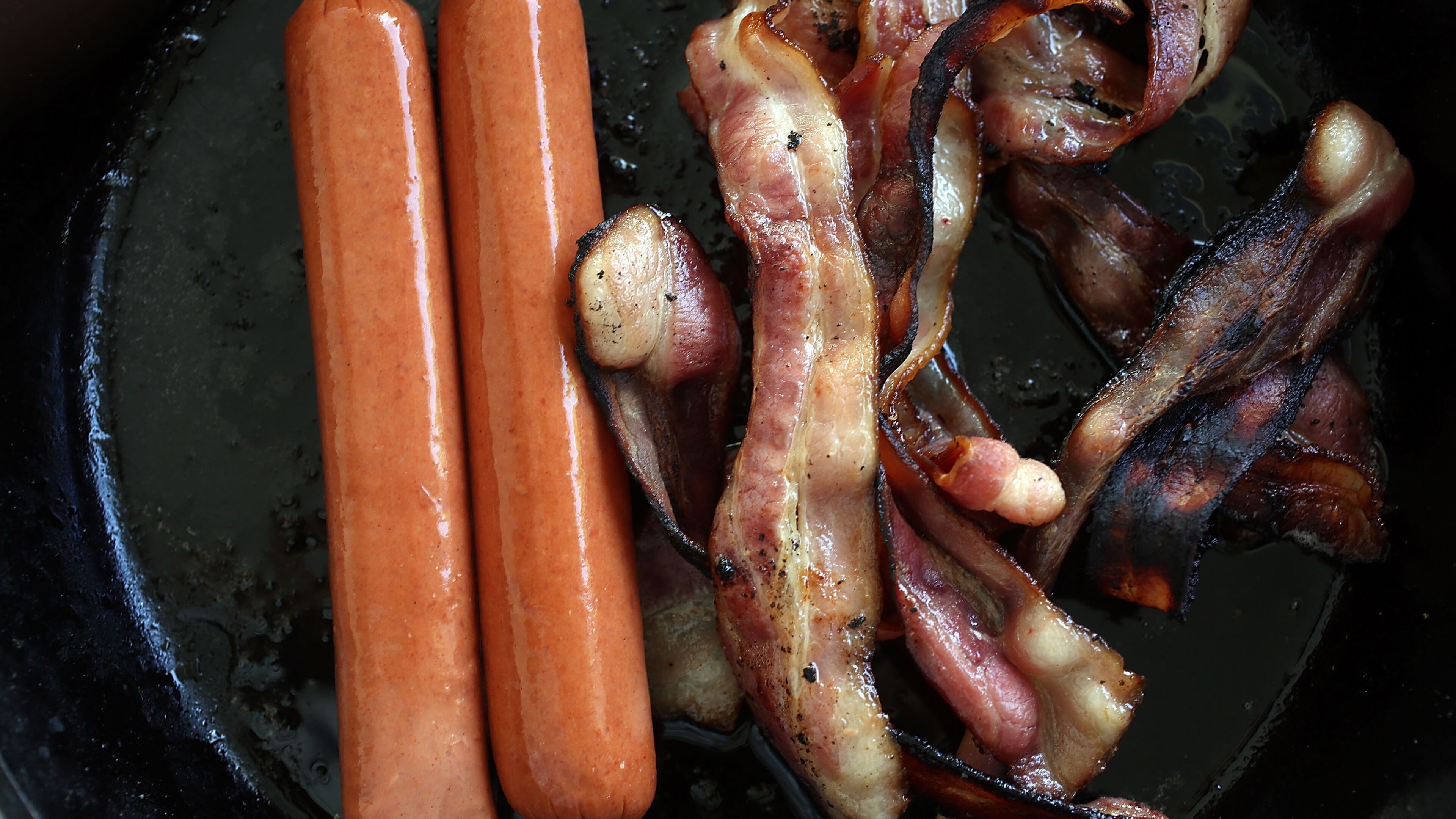 In this photo illustration, processed meats, including hot dogs and bacon, cook in a frying pan on October 26, 2015 in Miami, Florida. A report released today by the World Health Organization's International Agency for Research on Cancer announced that eating processed meat can lead to colorectal cancer in humans even as it remains a small chance but rises with the amount consumed. (Photo illustration by Joe Raedle/Getty Images)