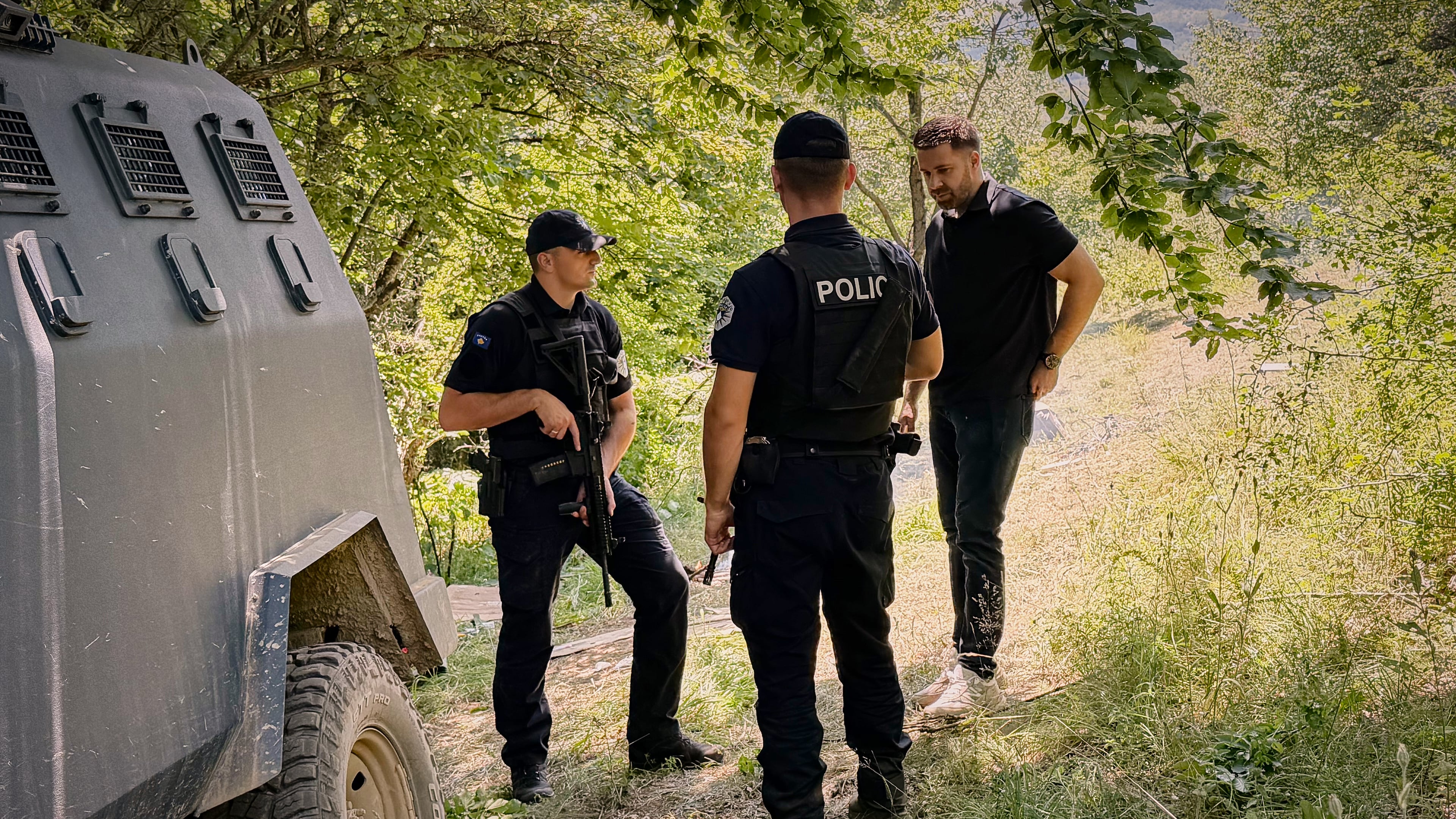 Erblin Ademi, right, whose father, Adem Ademi, a prominent surgeon, disappeared along with 22 other intellectuals during the Kosovo war in April 1999, speaks to police officers near the excavation site of a mass grave in Small Kalluder, Kosovo, Wednesday, Aug. 5, 2026. (AP Photo/Zana Cimili)