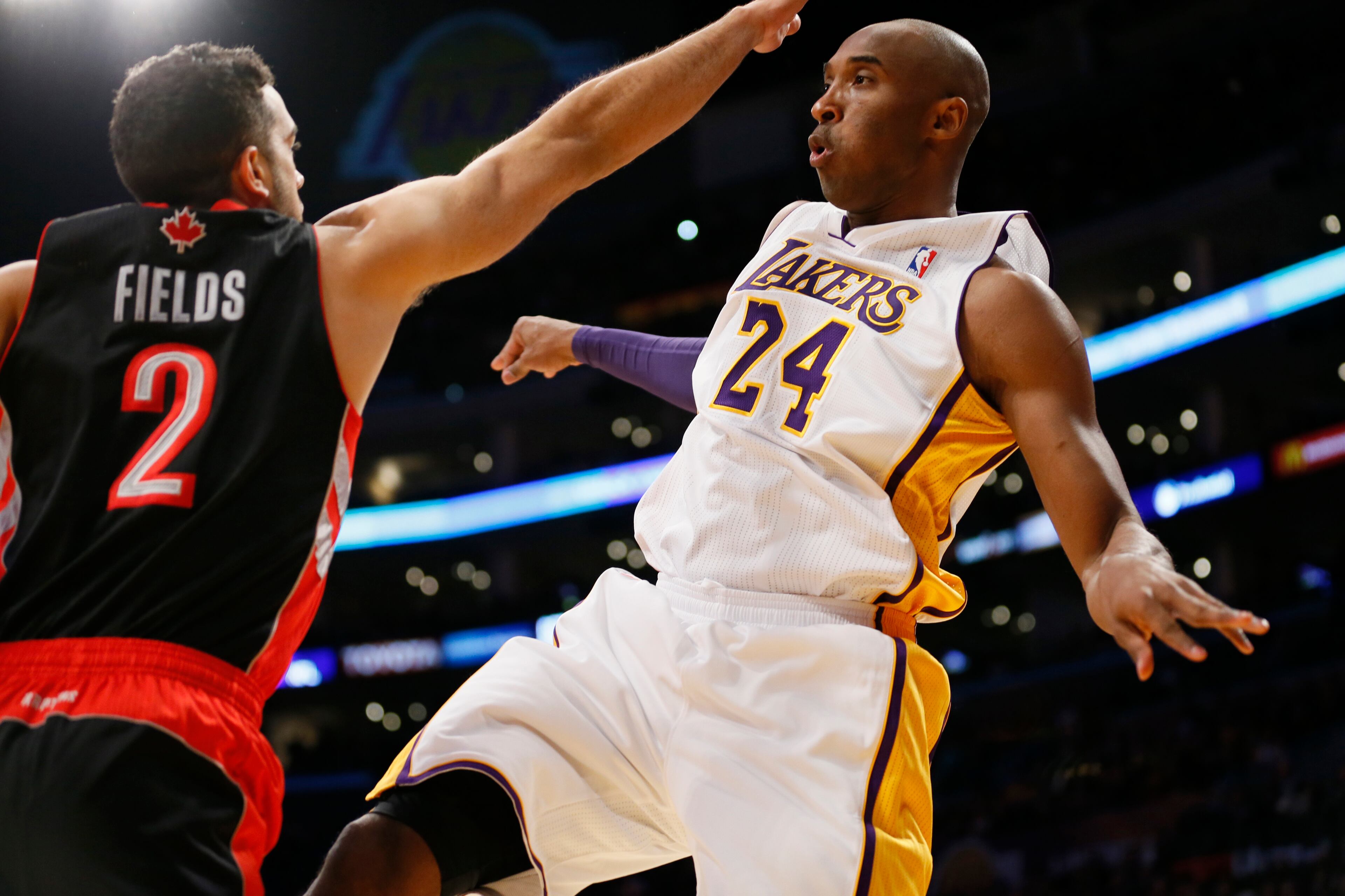 Los Angeles Lakers' Kobe Bryant, right, passes the ball over Toronto Raptors' Landry Fields, left, during the first quarter of an NBA basketball game in Los Angeles, Sunday, Dec. 8, 2013.