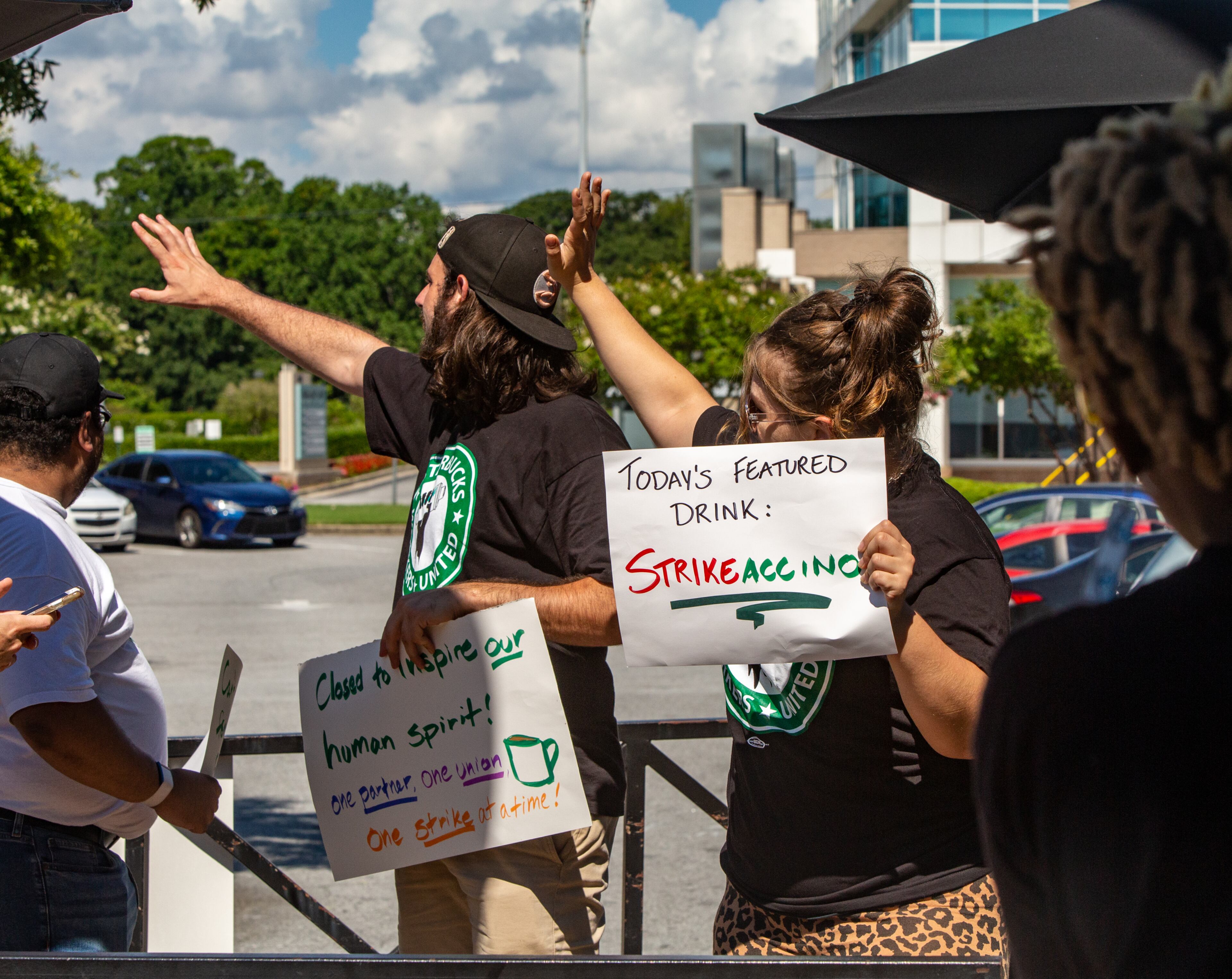 Starbucks employees, union workers and former Starbucks employees, including Nick Julian, far left, Camden Mitchell, center and Aleyah Riggs, right, picket at the Howell Mill location while on strike Sunday, July 17, 2022 after voting to join the union and asking for guaranteed work hours, benefits and a contract to protect the hourly workers. Starbucks management has not responded to requests to start negotiation. (Jenni Girtman for The Atlanta Journal-Constitution)
