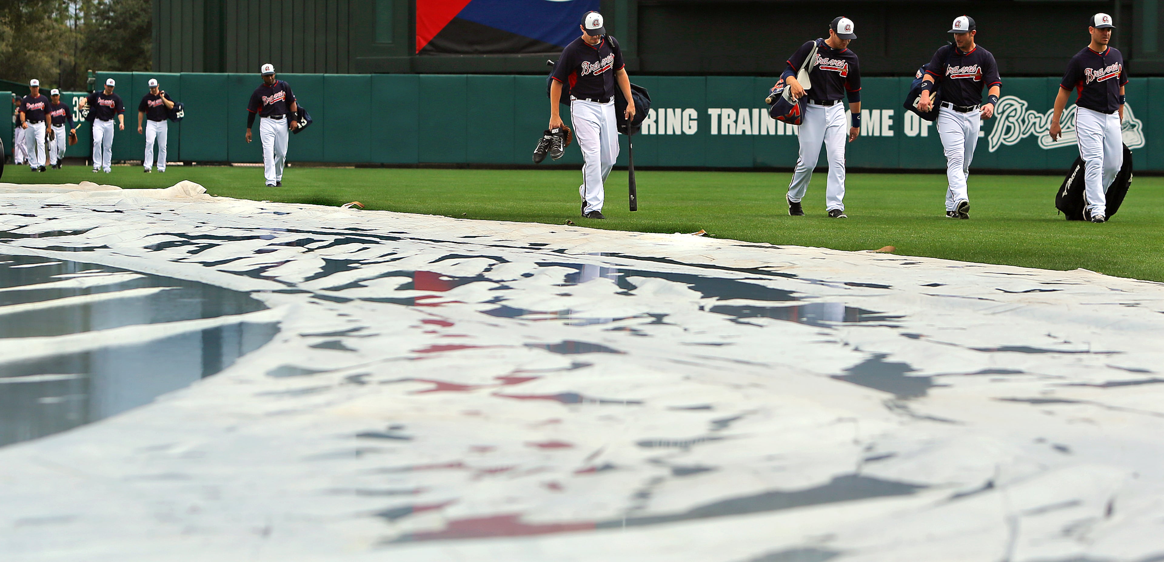 Braves players stream in to the clubhouse past the rain covered infield tarp at the conclusion of a rain shortened day of spring training practice on Friday, Feb. 21, 2014, in Lake Buena Vista, FL. Due to inclement weather all players, coaches, and fans were asked to clear the fields when thunder storms moved through the area forcing players into the batting tunnels for the day.