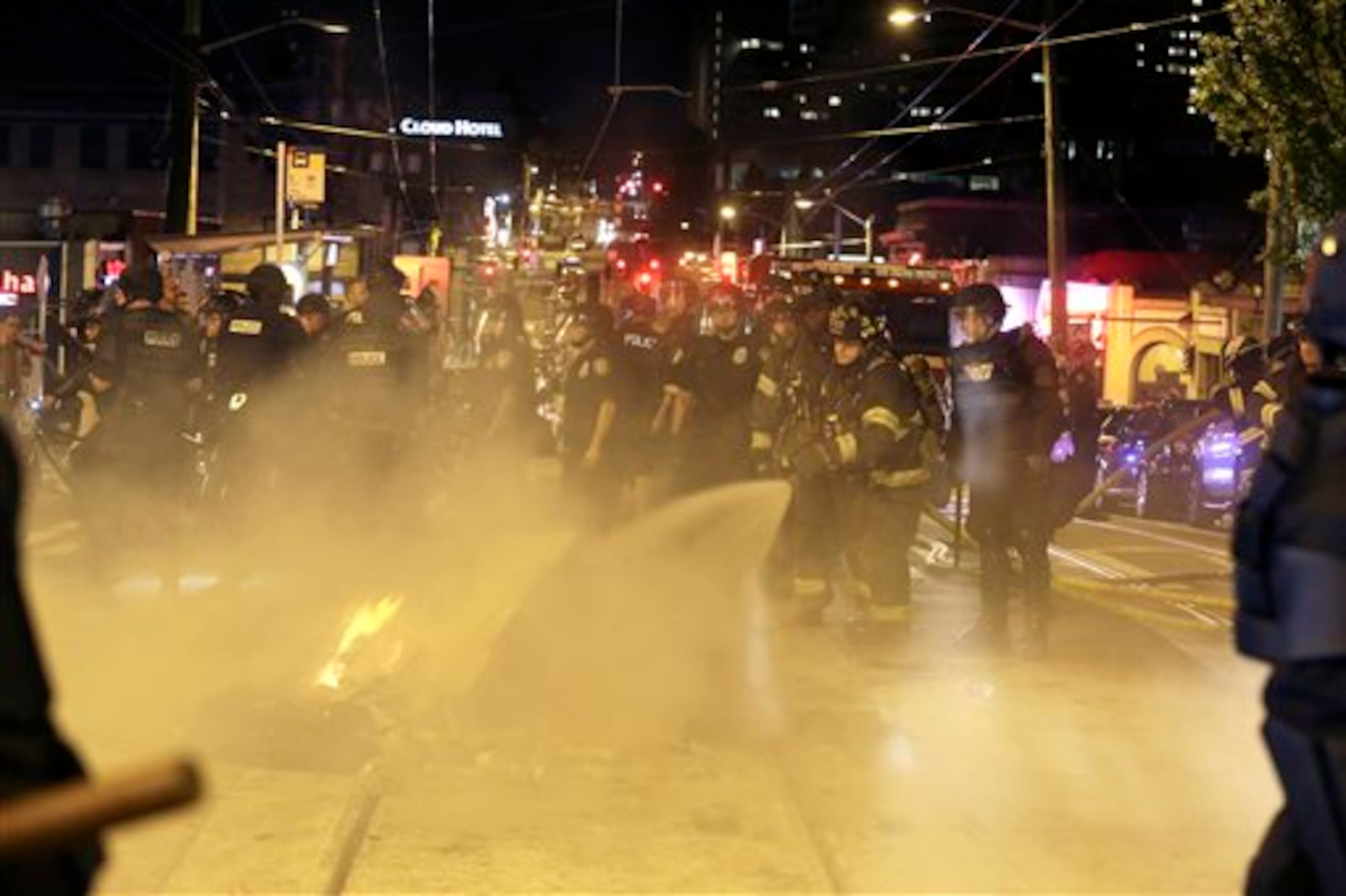 Fire fighters extinguish a fire during May Day activities Thursday, May 1, 2014 in Seattle. Police have made several arrests and fired pepper spray as anti-capitalist marchers meandered through Seattle several hours after hundreds of peaceful demonstrators took part in a May Day march in support of immigrant rights and a boost in the minimum wage. (AP Photo/Ted S. Warren)