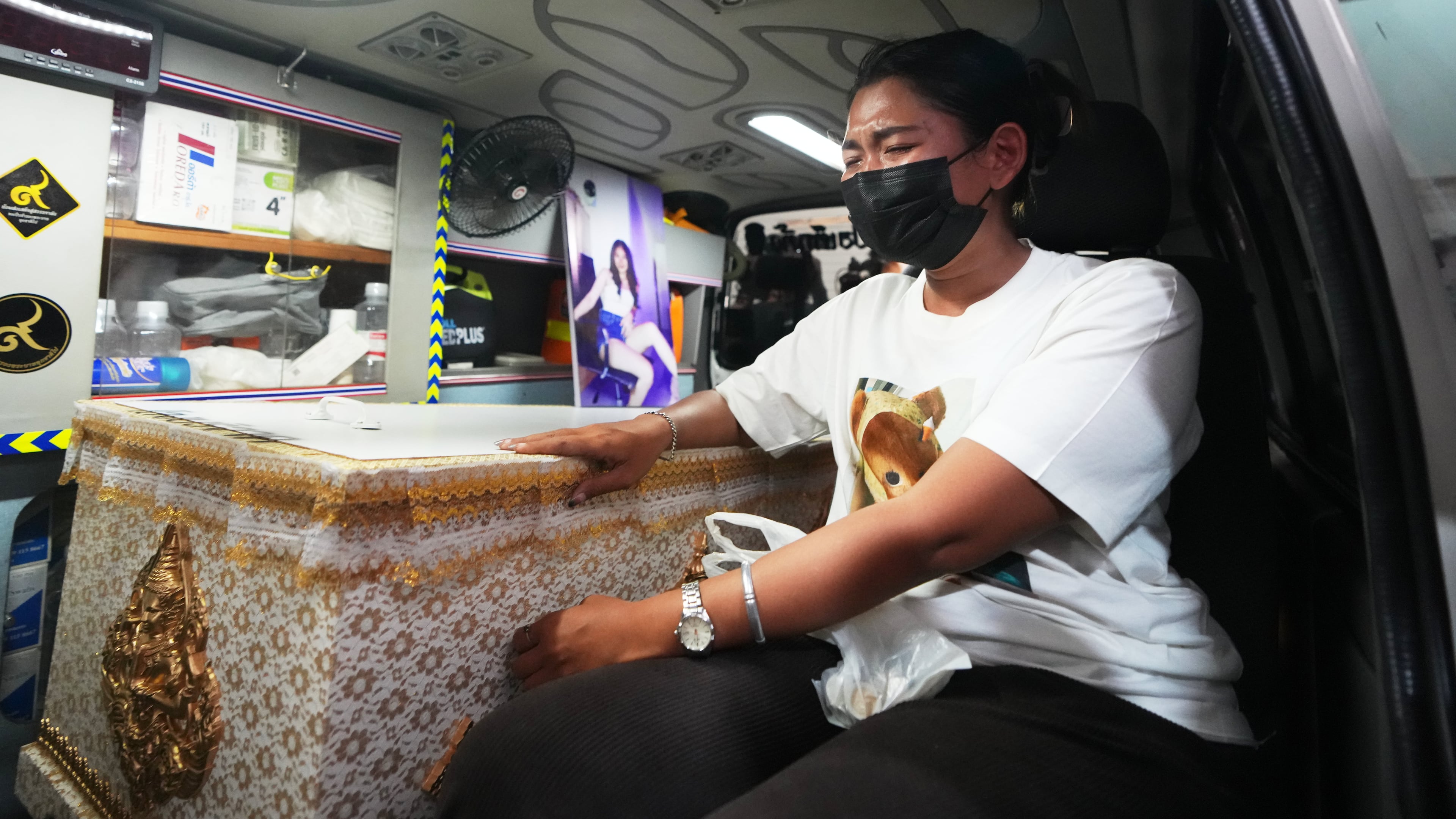 A relative of a victim in a music bar fire sits near the coffin containing the victim's body inside a vehicle as it is transferred from a police hospital in Bangkok, Thailand, Wednesday, July 15, 2026, (AP Photo/Sakchai Lalit)