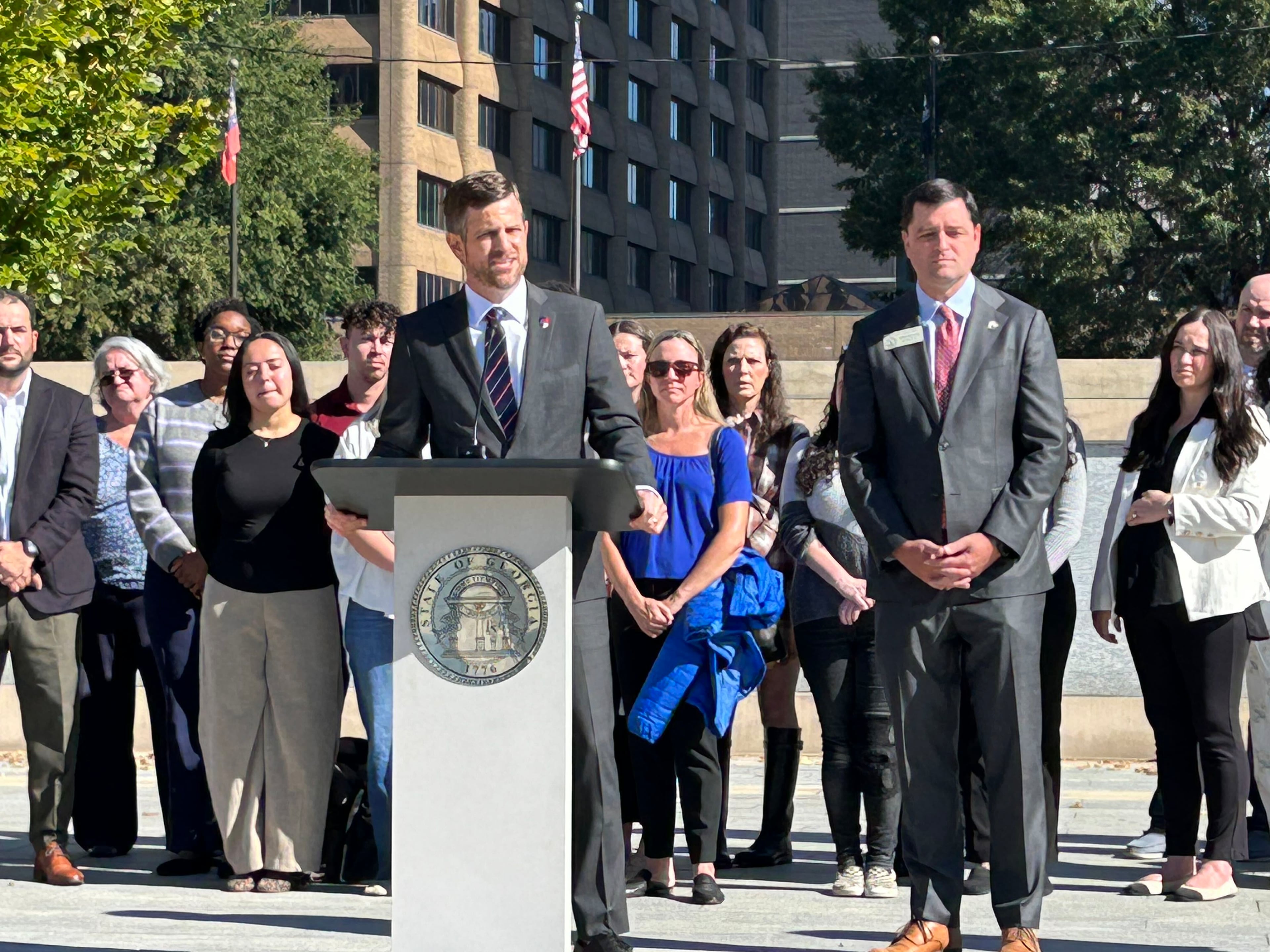 State Sen. Brian Strickland (at lectern) speaks during a news conference while state Rep. Scott Hilton listens outside the state Capitol on Thursday. (David Wickert/AJC)