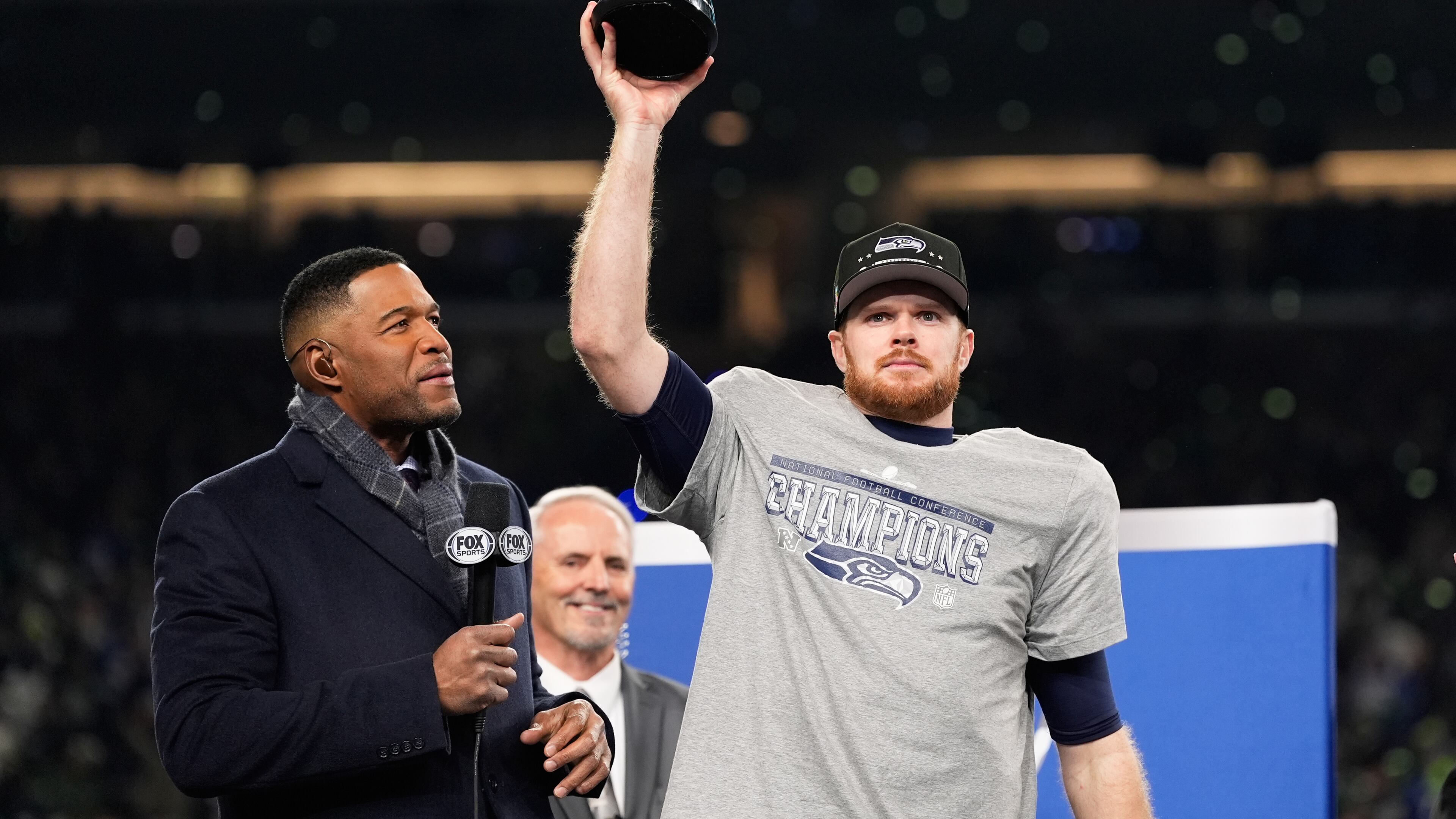 Seattle Seahawks quarterback Sam Darnold lifts the winner's trophy next to Michael Strahan, left, after a win over the Los Angeles Rams in the NFC Championship NFL football game Sunday, Jan. 25, 2026, in Seattle. (AP Photo/Godofredo A. Vásquez)