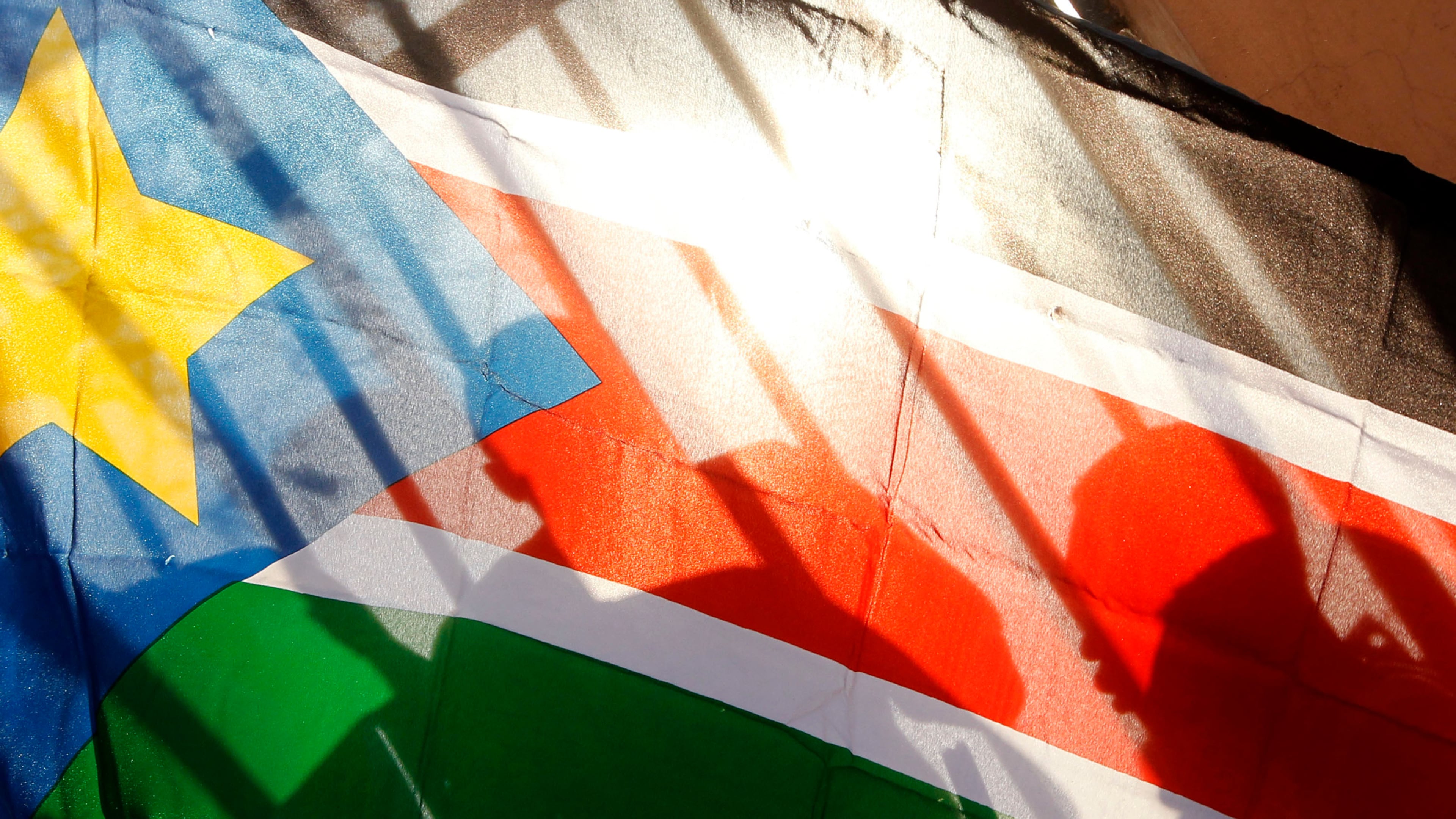 FILE - The silhouettes of South Sudanese people are seen through a South Sudanese flag as they line up to cast their votes in Juba, South Sudan, Jan. 9, 2011. (AP Photo/Jerome Delay, File)