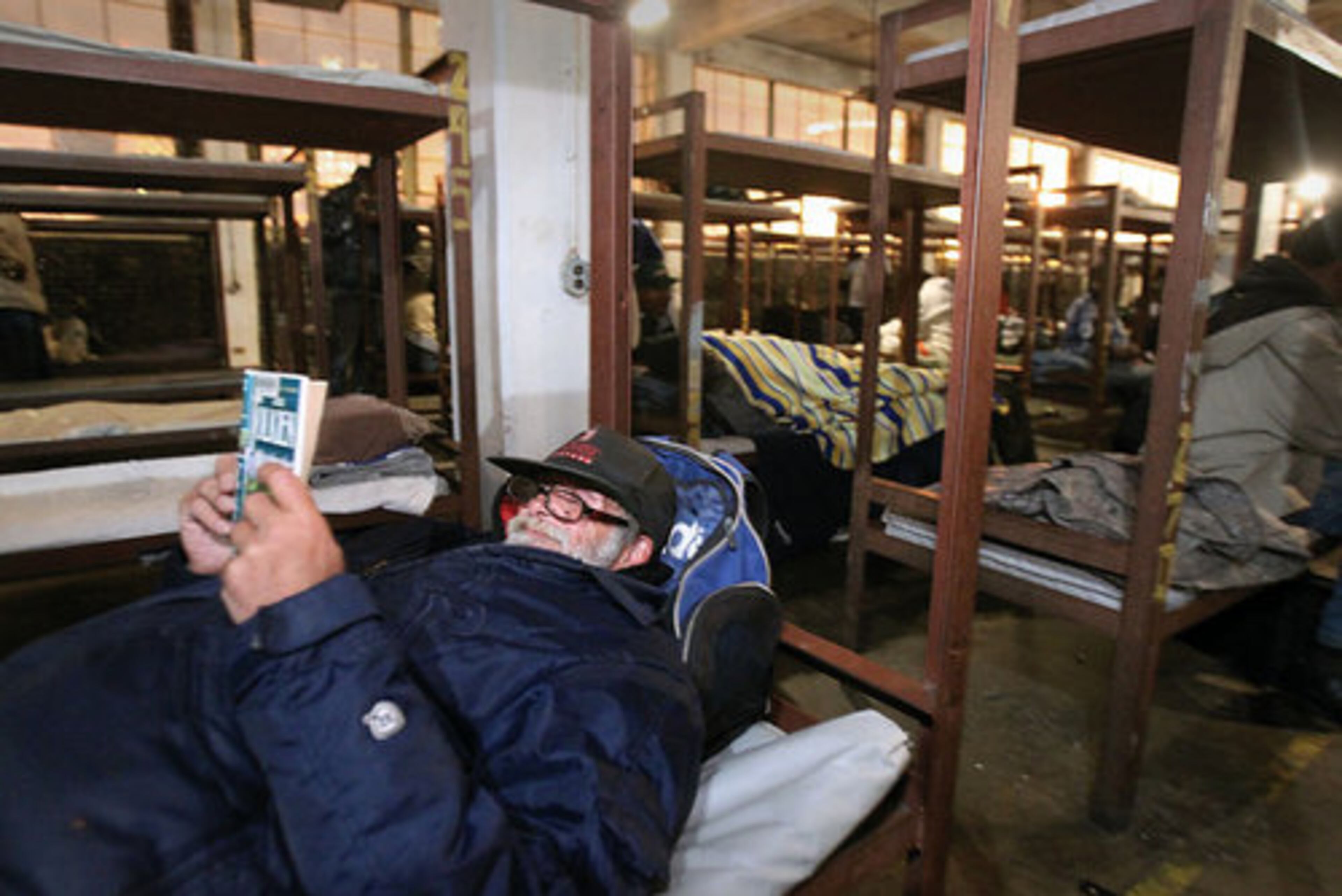 After the 7 p.m. curfew, Richard Stillmank, 60, reads his book by J.R.R. Tolkien in a bed in room No. 1, which has about 400 bunk beds.