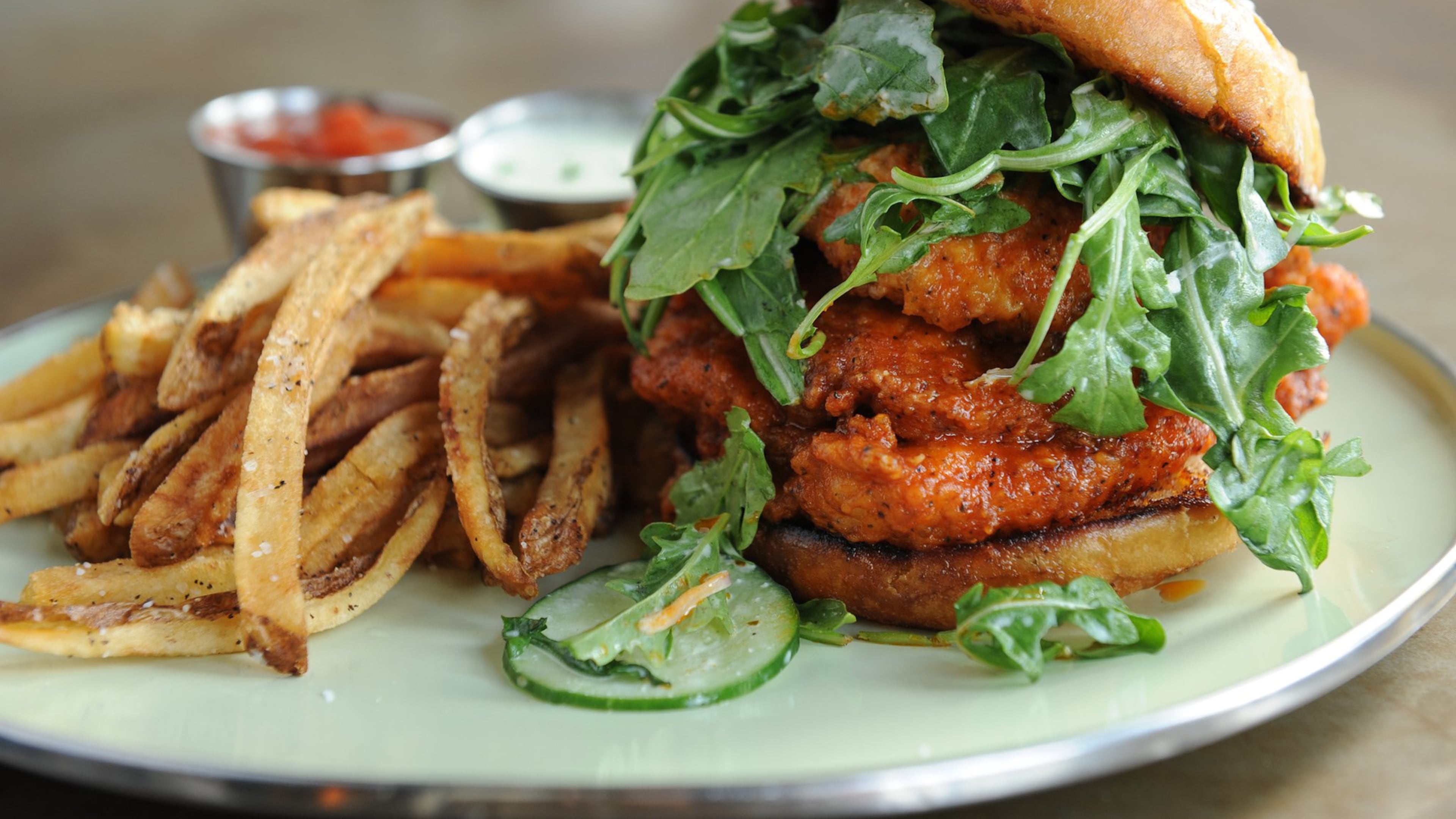 The Spicy Chicken Sammy at Rising Son has Sriracha Buffalo sauce, cucumber, arugula, ranch, onion bun and fries. (BECKY STEIN PHOTOGRAPHY)