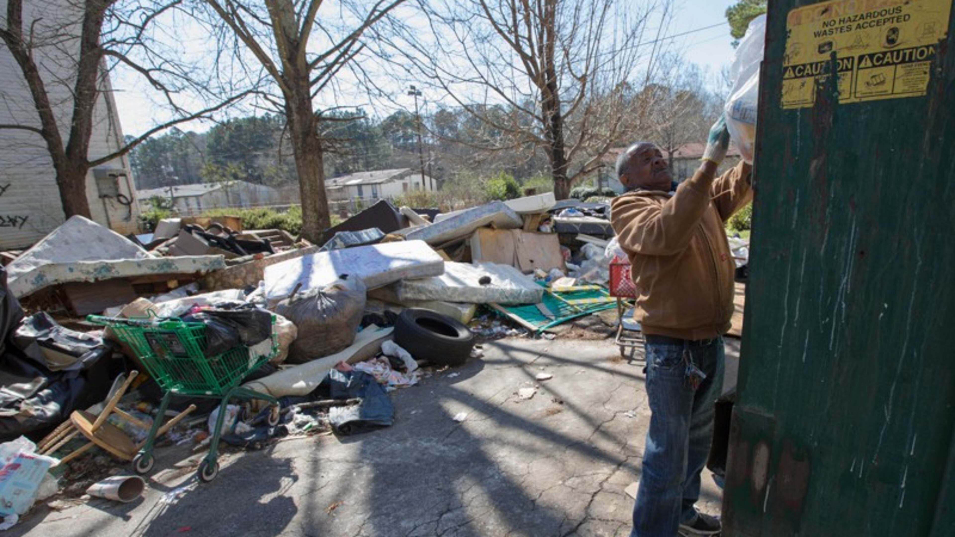 In this photo from February 2016, resident James Starr, who had lived at Brennon Hill for four years, puts his trash in a Dumpster despite trash and debris everywhere on the property. The site was later condemned and now the demolition will be complete. AJC file photo