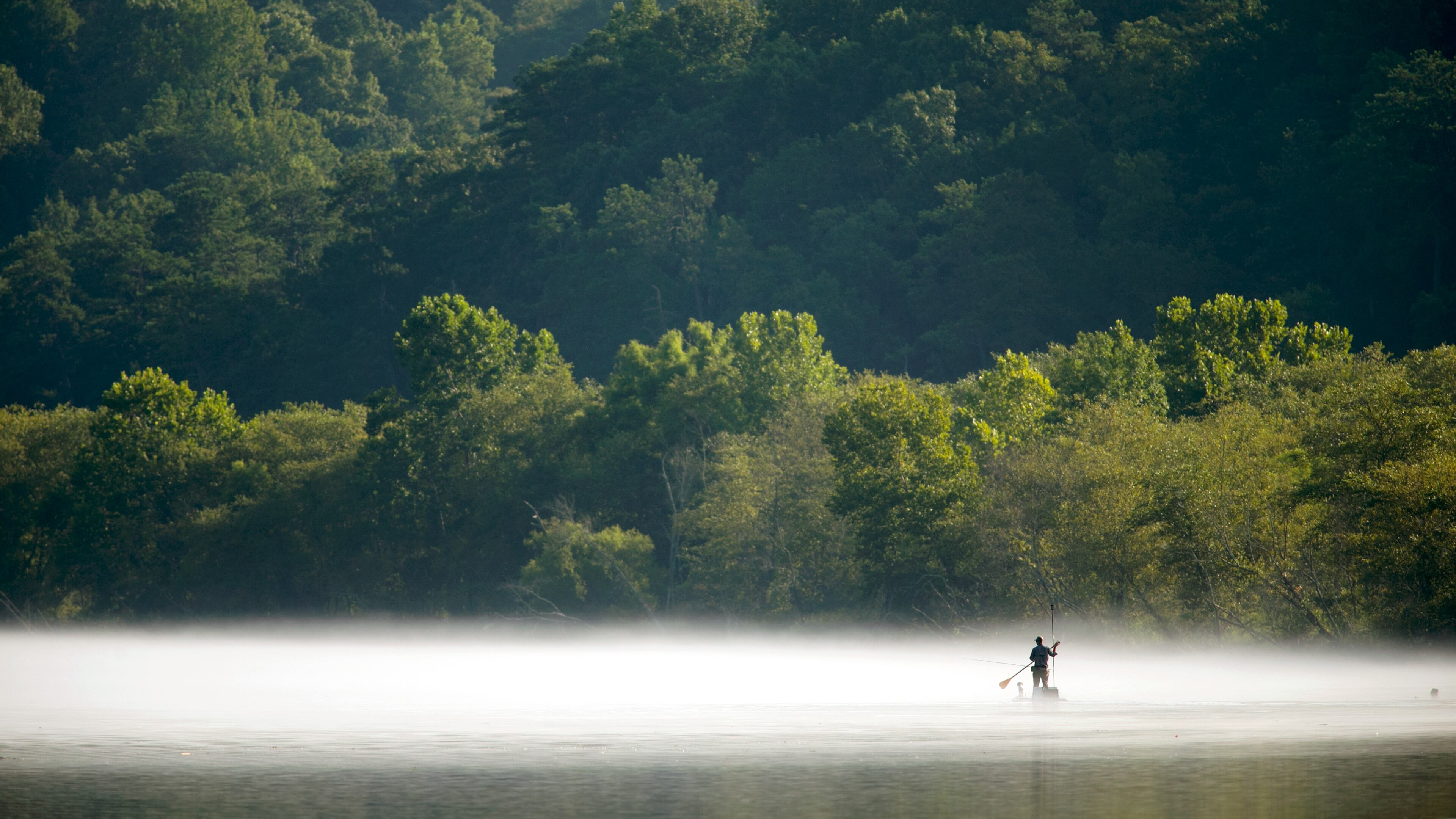 A fisherman paddles through the fog on a paddle board to fish on the Chattahoochee River at Morgan Falls Overlook Park Sunday, July 19, 2015.