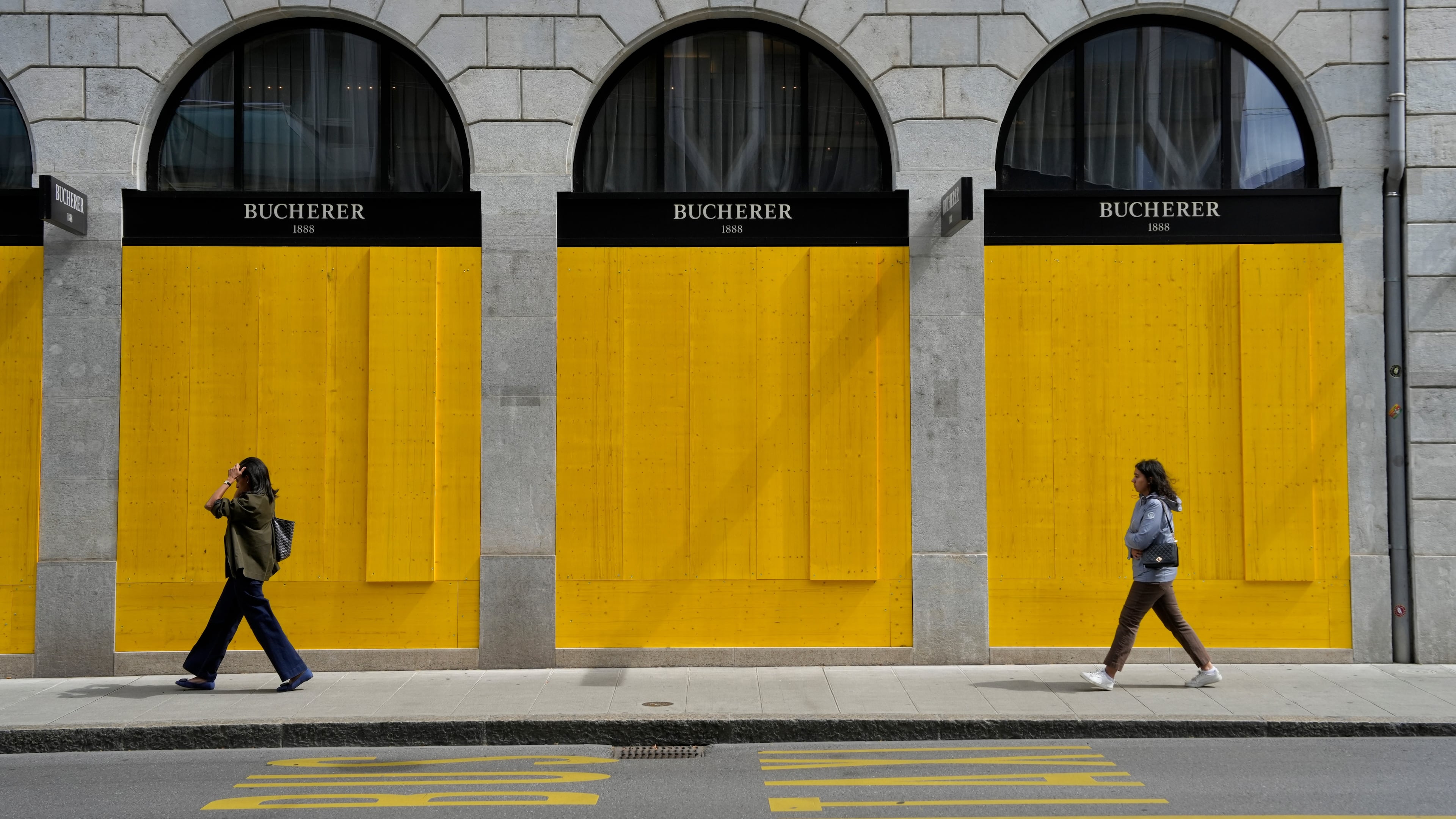 Pedestrians walk past the boarded-up windows of a shop, ahead of expected protests for the G7 summit, in Geneva, Switzerland, Tuesday, June 9, 2026. (AP Photo/Baz Ratner)