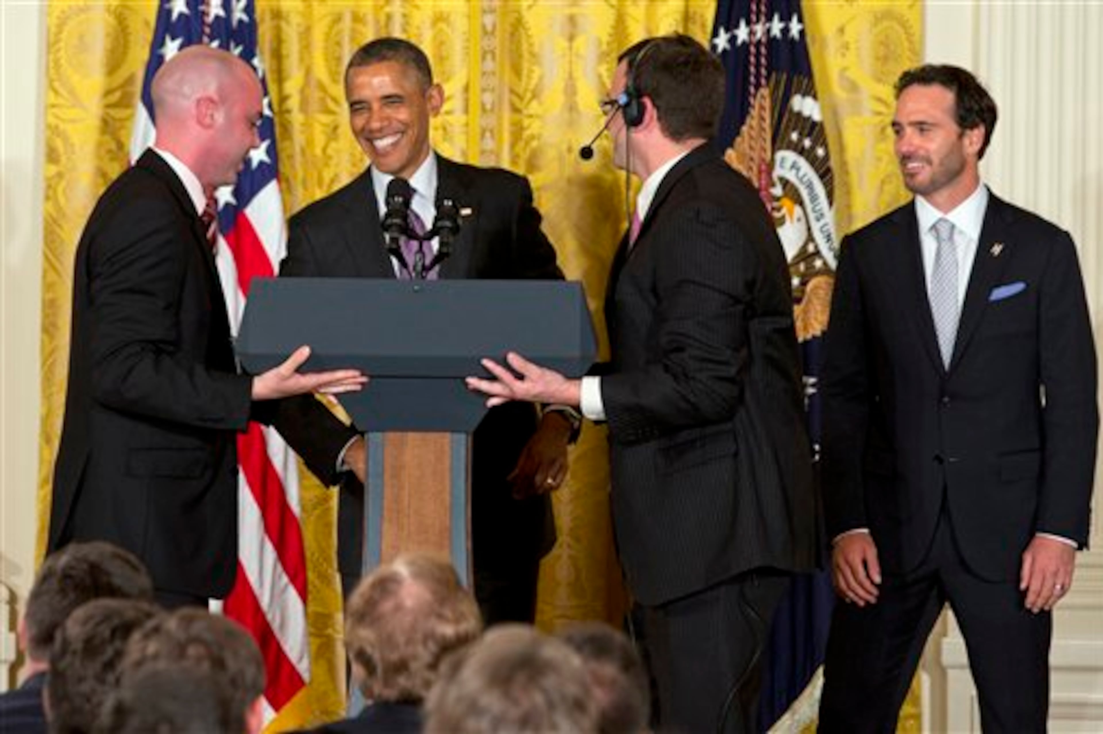 President Barack Obama laughs as he jokes that the White House staff moving the podium from the stage are his "pit crew," next to NASCAR driver Jimmie Johnson, right, of Hendrick Motorsports, during a ceremony honoring the 2013 NASCAR Sprint Cup Series champions, Wednesday, June 25, 2014, in the East Room of the White House in Washington. (AP Photo/Jacquelyn Martin)