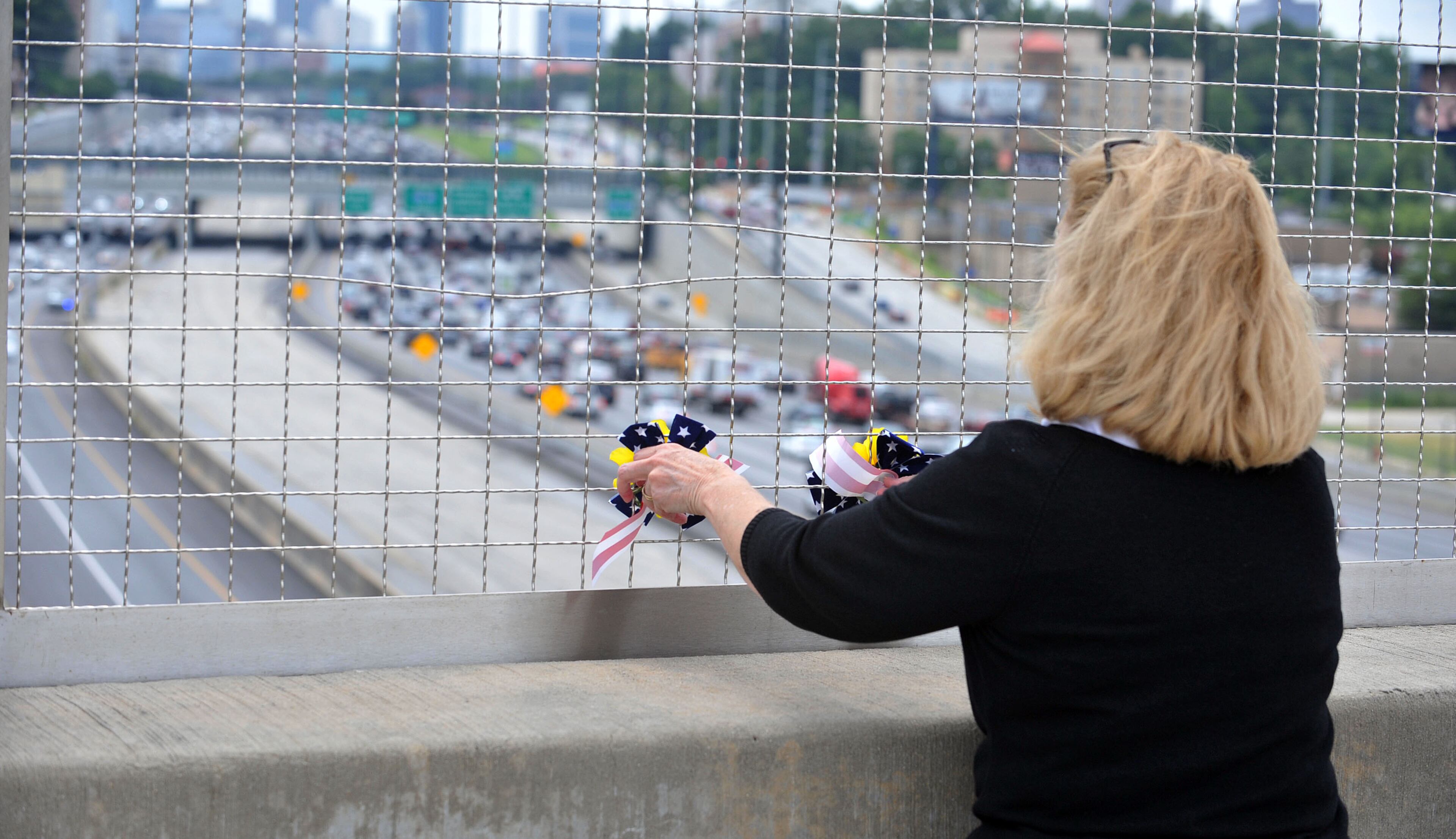 Donna Durrett, of Ellijay, places flowers in a fence on the 17th Street bridge over-looking the highway. A motorcade shuts down the Downtown Connector northbound as the body of Marine Corps Lance Cpl. Skip Wells was escorted from Hartsfield-Jackson International Airport Thursday, July 23, 2015. The Marietta Police Department shut down a portion of the Canton Road Connector Bridge over Interstate 75, so that the City and citizens could gather on the roadway to pay their respects to Lance Corporal Wells and the other Marines and Sailor who were killed in Chattanooga in the line of duty in a terrorist shooting last week. KENT D. JOHNSON /KDJOHNSON@AJC.COM