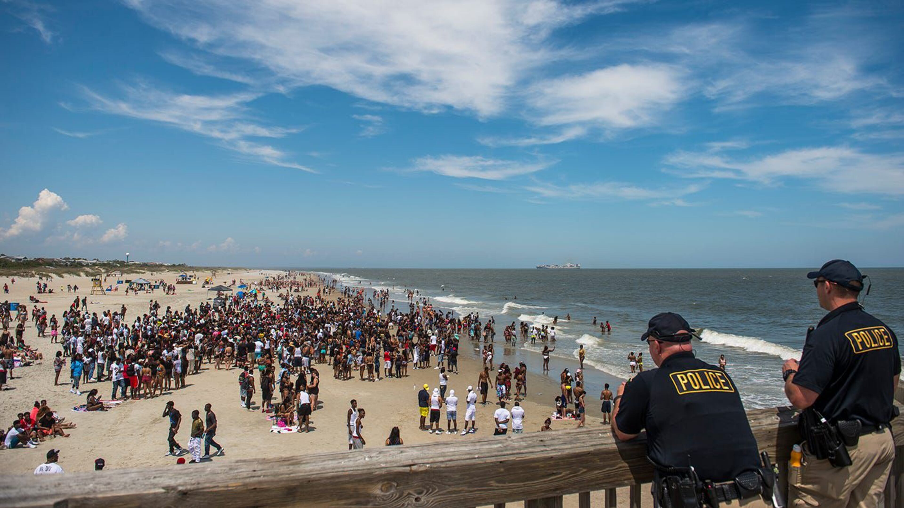 Police officers watch a crowd of partiers gather on the beach for Orange Crush Saturday afternoon at Tybee Island. Police are investigating several incidents, including the attack of two women Sunday at the beach.