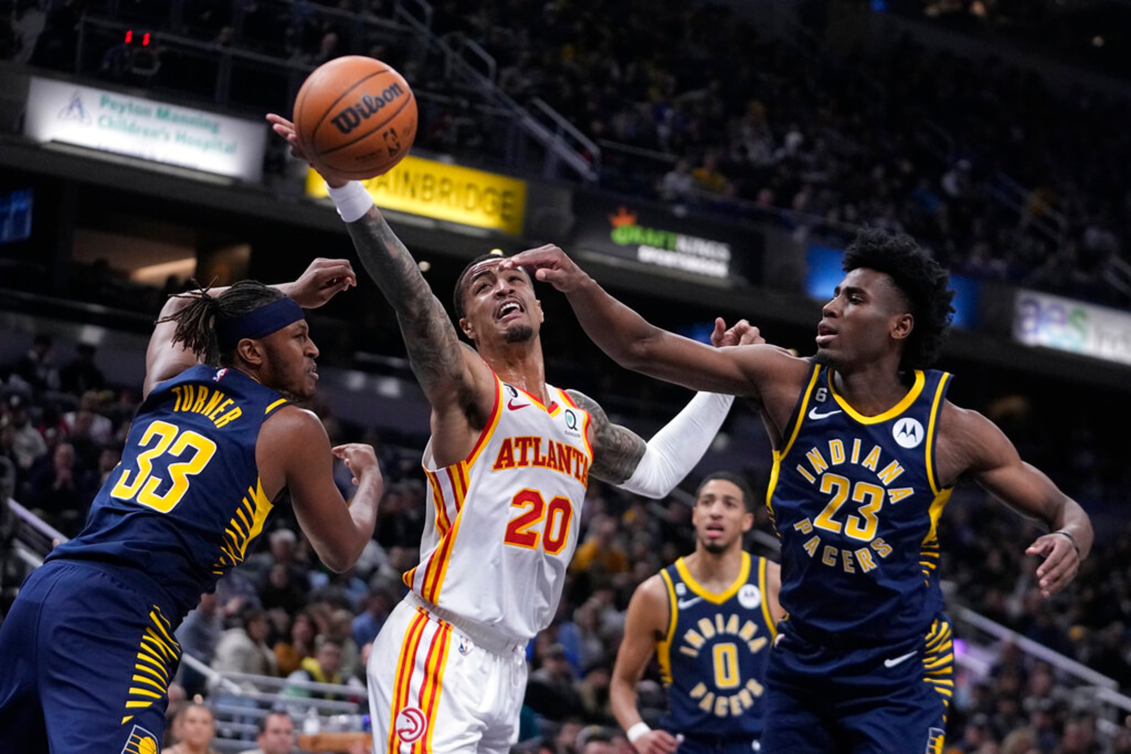 Atlanta Hawks' John Collins (20) reaches for a rebound between Indiana Pacers' Myles Turner (33) and Aaron Nesmith (23) during the first half of an NBA basketball game Tuesday, Dec. 27, 2022, in Indianapolis. (AP Photo/Darron Cummings)