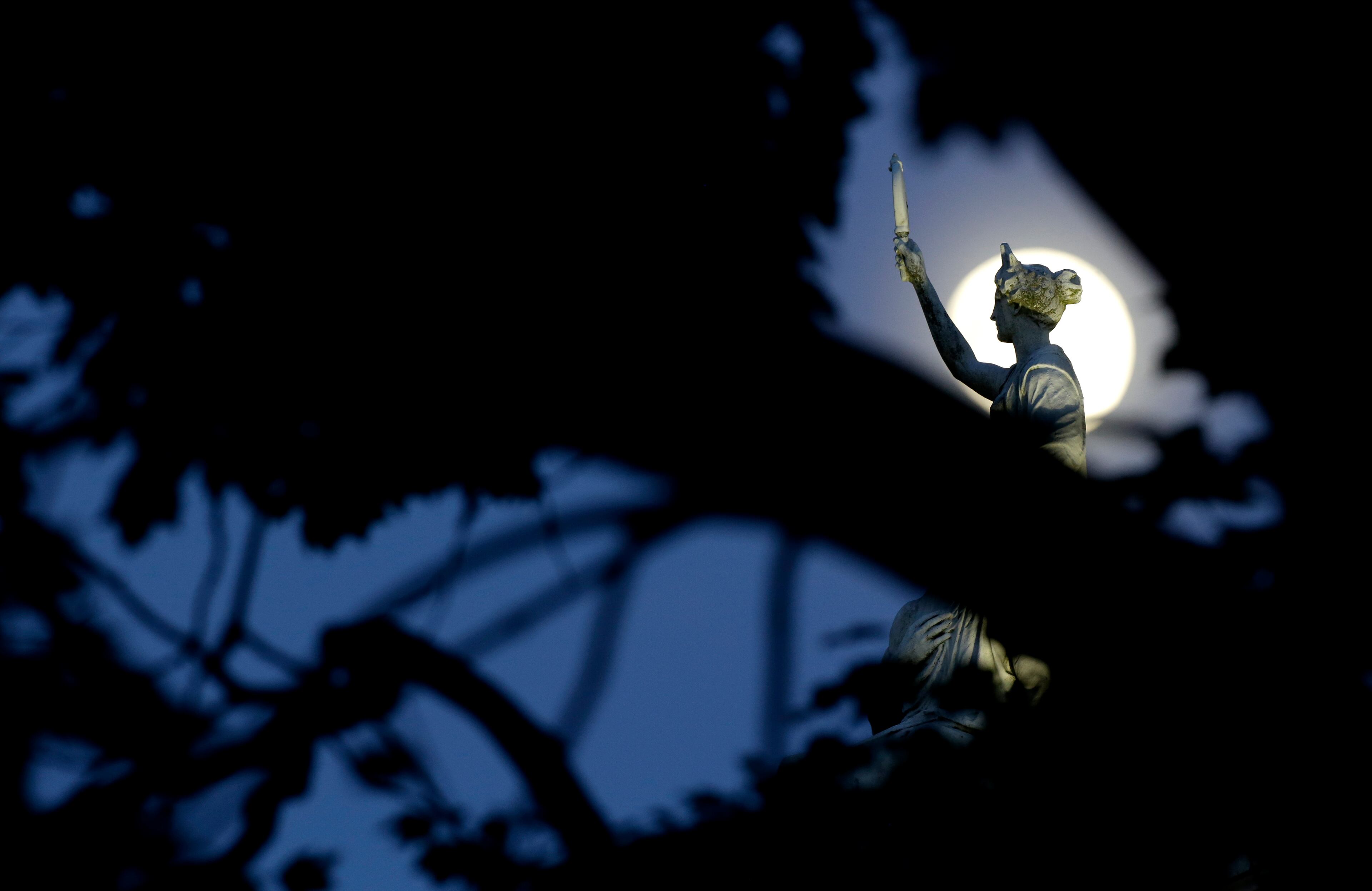 The moon in its waxing gibbous stage sh behind tree limbs and a statue a marble statue by John Gelert representing history and law on the top of the Bergen County Courthouse in Hackensack, N.J., Friday, June 21, 2013. The moon, which will reach its full stage on Sunday, is expected to be 13.5 percent closer to earth during a phenomenon known as supermoon. (AP Photo/Julio Cortez)