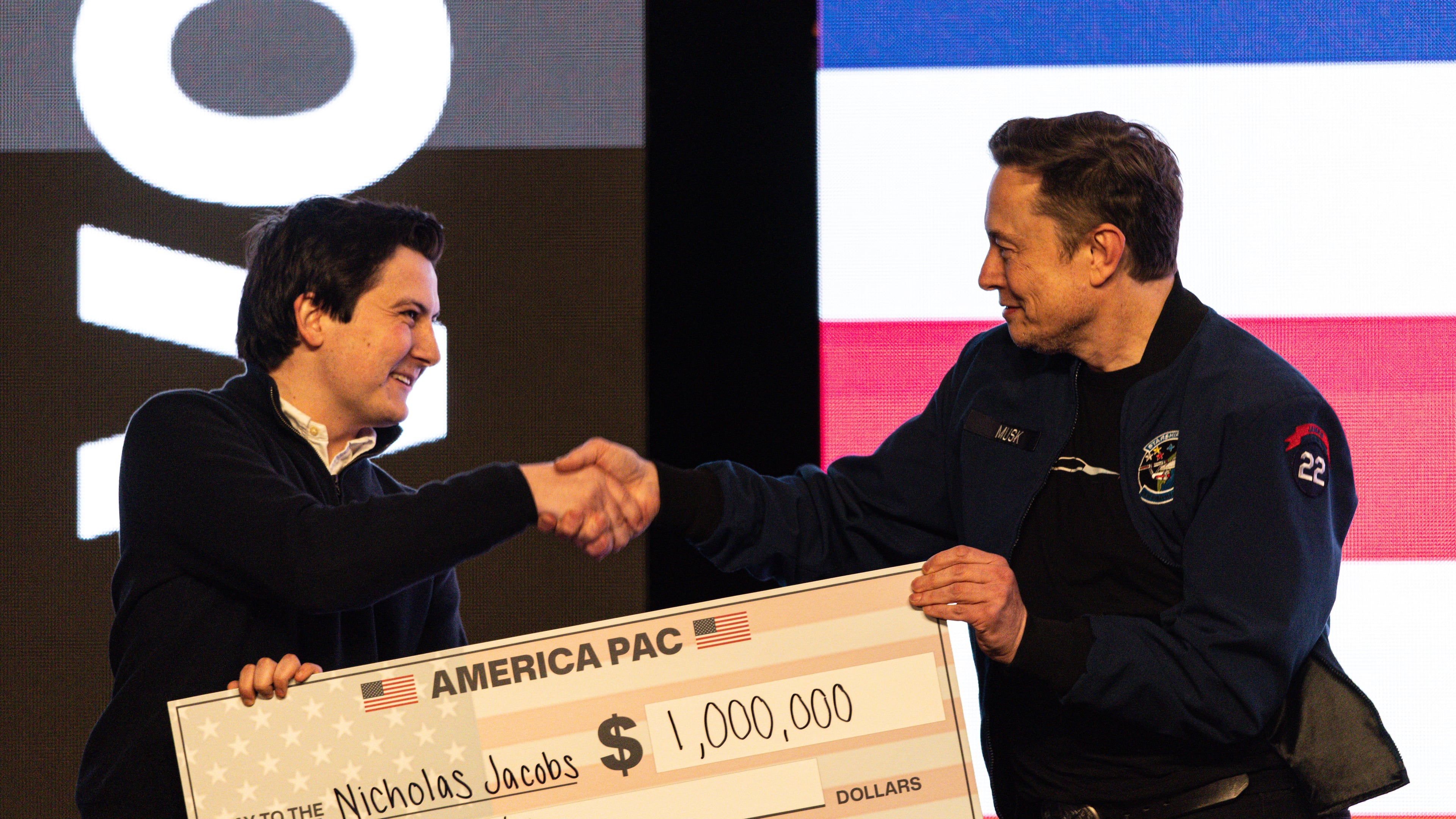FILE - Elon Musk hands over a million dollar check to Nicholas Jacobs during a town hall in Green Bay, Wis., March 30, 2025. (AP Photo/Jeffrey Phelps, File)