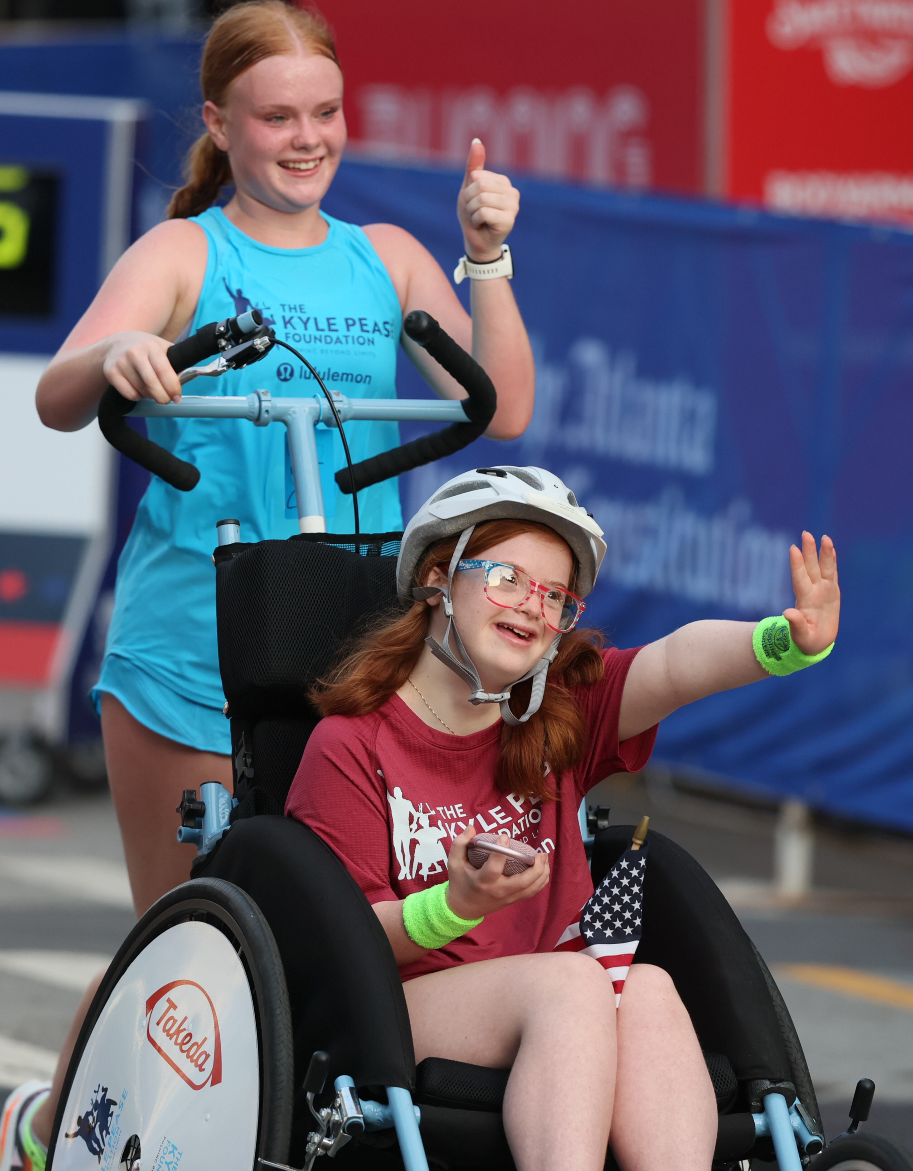 Darden Glass being pushed by sister Anna Glass crosses the finish line at the 55th running of the Atlanta Journal-Constitution Peachtree Road Race in Atlanta on Thursday, July 4, 2024. (Jason Getz / AJC)