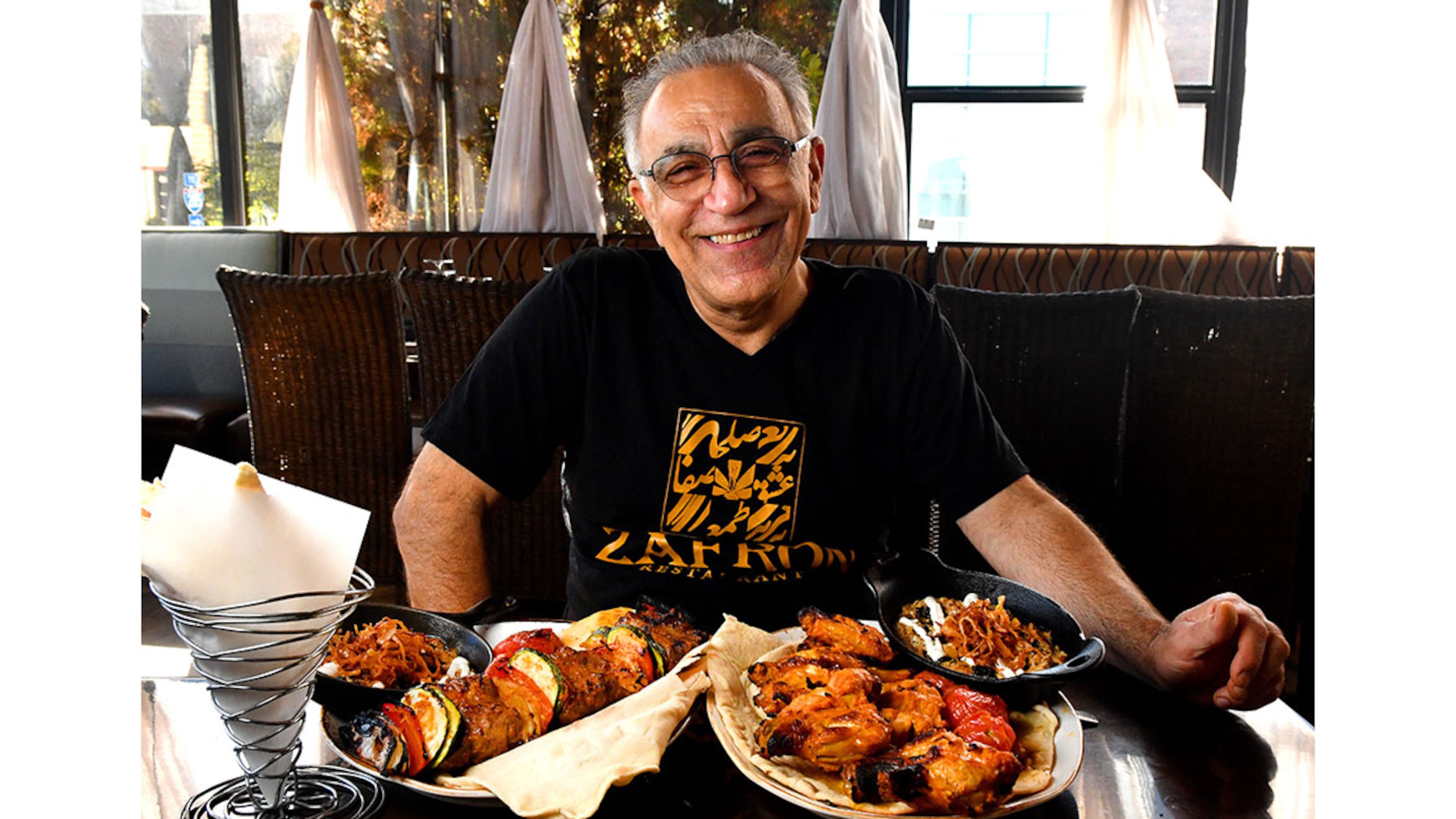 Peter Teimori, chef and owner of Zafron Restaurant in Sandy Springs, poses for a portrait with his (from left) bread, Kashk Bademjoon (eggplant spread with crispy mint and fried onions), Beef Shish Kebabs with grilled vegetables, Zafron Wings with grilled tomatoes, and a second serving of Kashk Bademjoon. (Styling by Peter Teimori / Chris Hunt for the AJC)