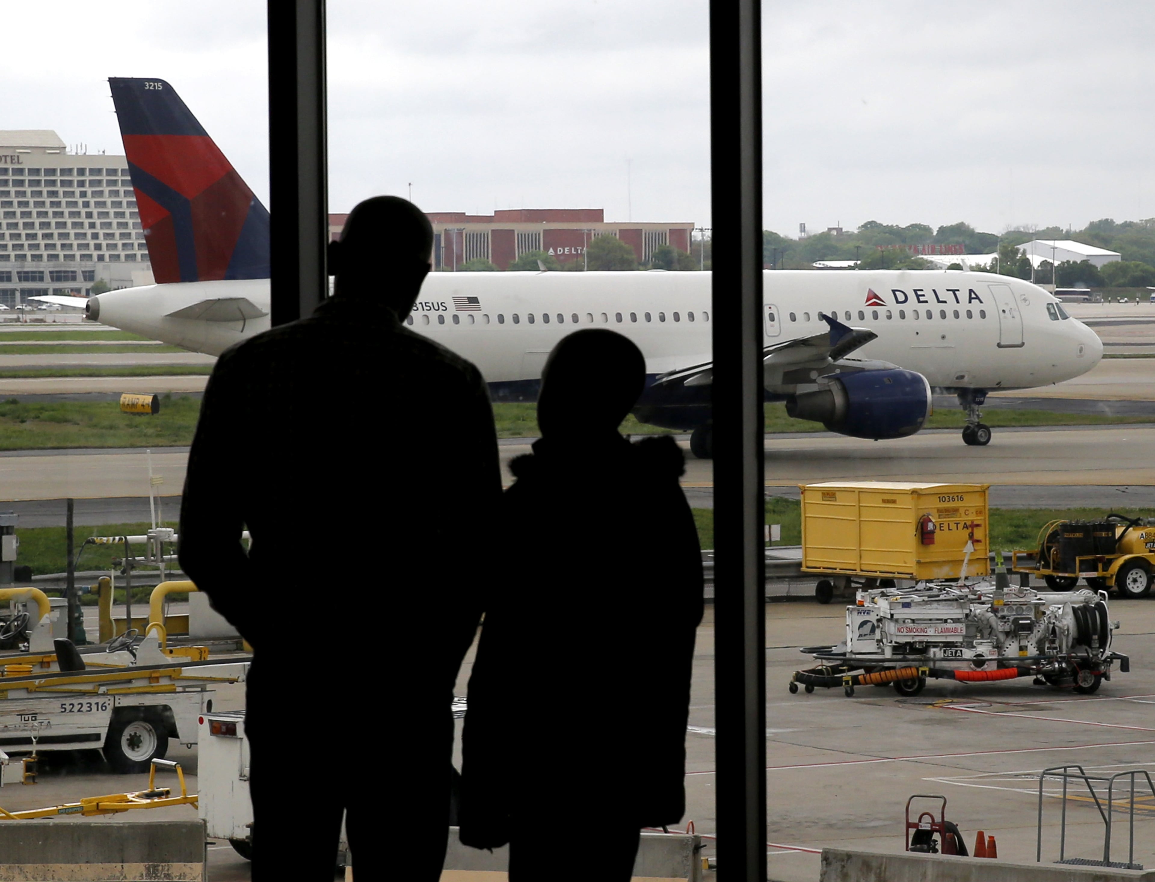 In this Tuesday, April 14, 2015 photo, travelers watch as a plane taxis at Hartsfield-Jackson Atlanta International Airport in Atlanta. After years of steadily-rising airfare, travelers this summer can expect a tiny bit of relief, a really tiny bit. The average roundtrip domestic ticket this summer now stands at $454, down $2.01 from last summer. Vacationers to Europe will fare better with tickets down 3 percent to $1,619, about $50 less. (AP Photo/Charles Rex Arbogast)