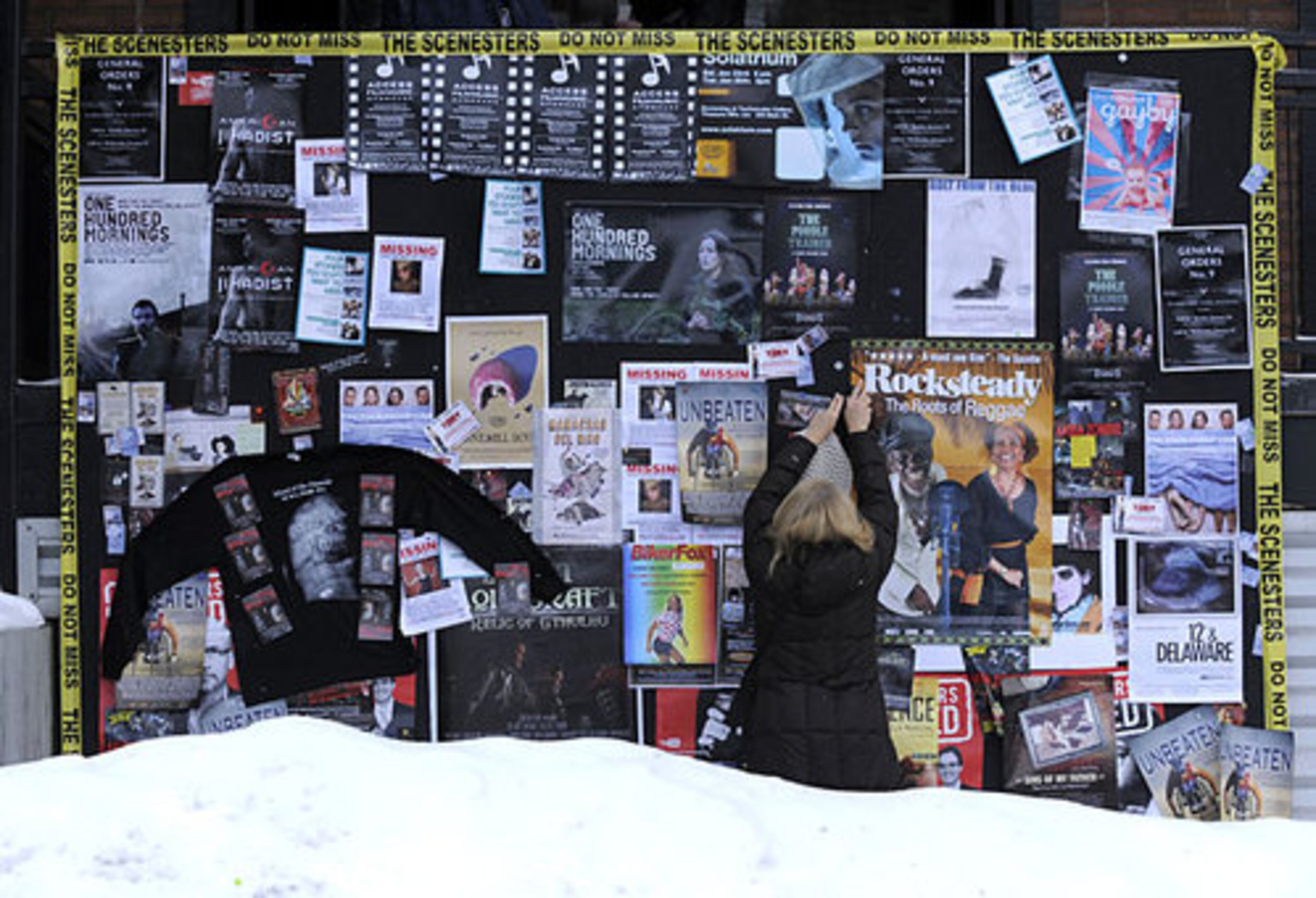 Betty Palik, producer of the film "Rocksteady: The Roots of Reggae, " puts up a poster for her film on a crowded bulletin board on Main Street.