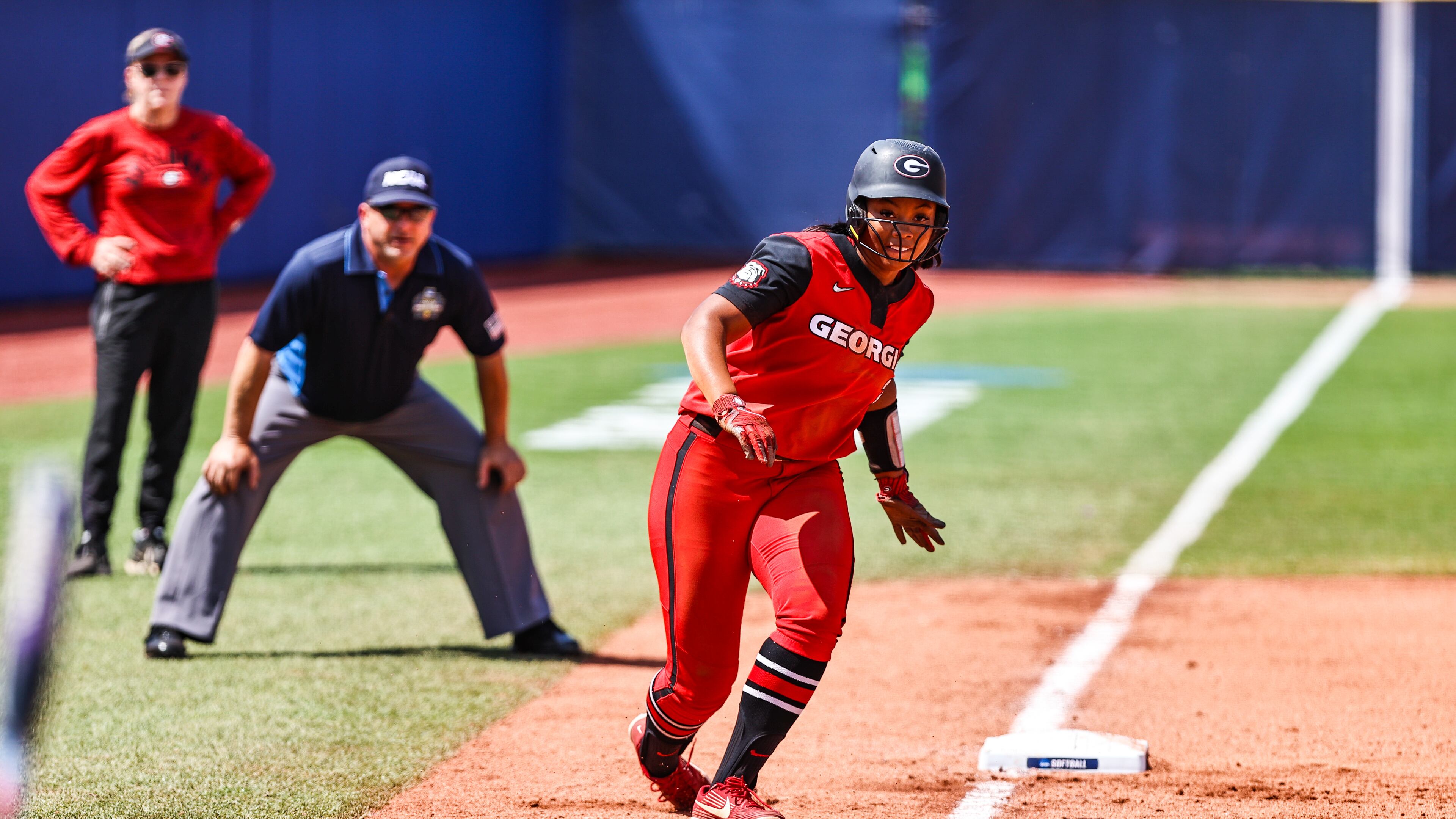 Georgia outfielder Jaiden Fields (3) takes a lead at third base as coach Lu Harris-Champer (l) looks on in the background. Fields scored a run for Georgia, but the third-base coaching decisions cost the Bulldogs one run and possibly two in a 3-2 loss to No. 5 Oklahoma State on Tuesday, June 3, 2021, in Oklahoma City. (Photo by Tony Walsh)