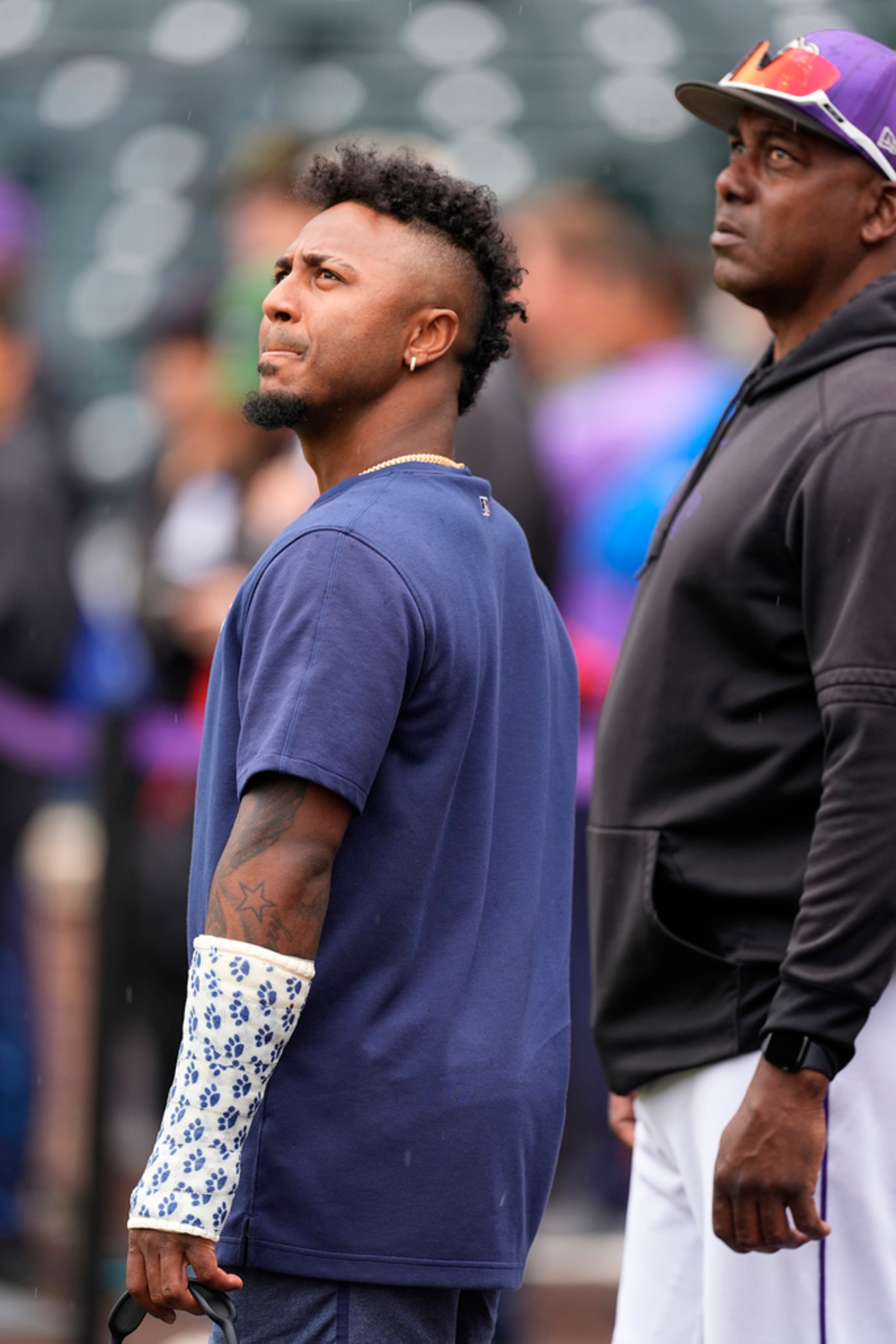 Injured Atlanta Braves second baseman Ozzie Albies, left, looks on with Colorado Rockies hitting coach Hensley Meulens, right, as players warm up before a baseball game Friday, Aug. 9, 2024, in Denver. (AP Photo/David Zalubowski)